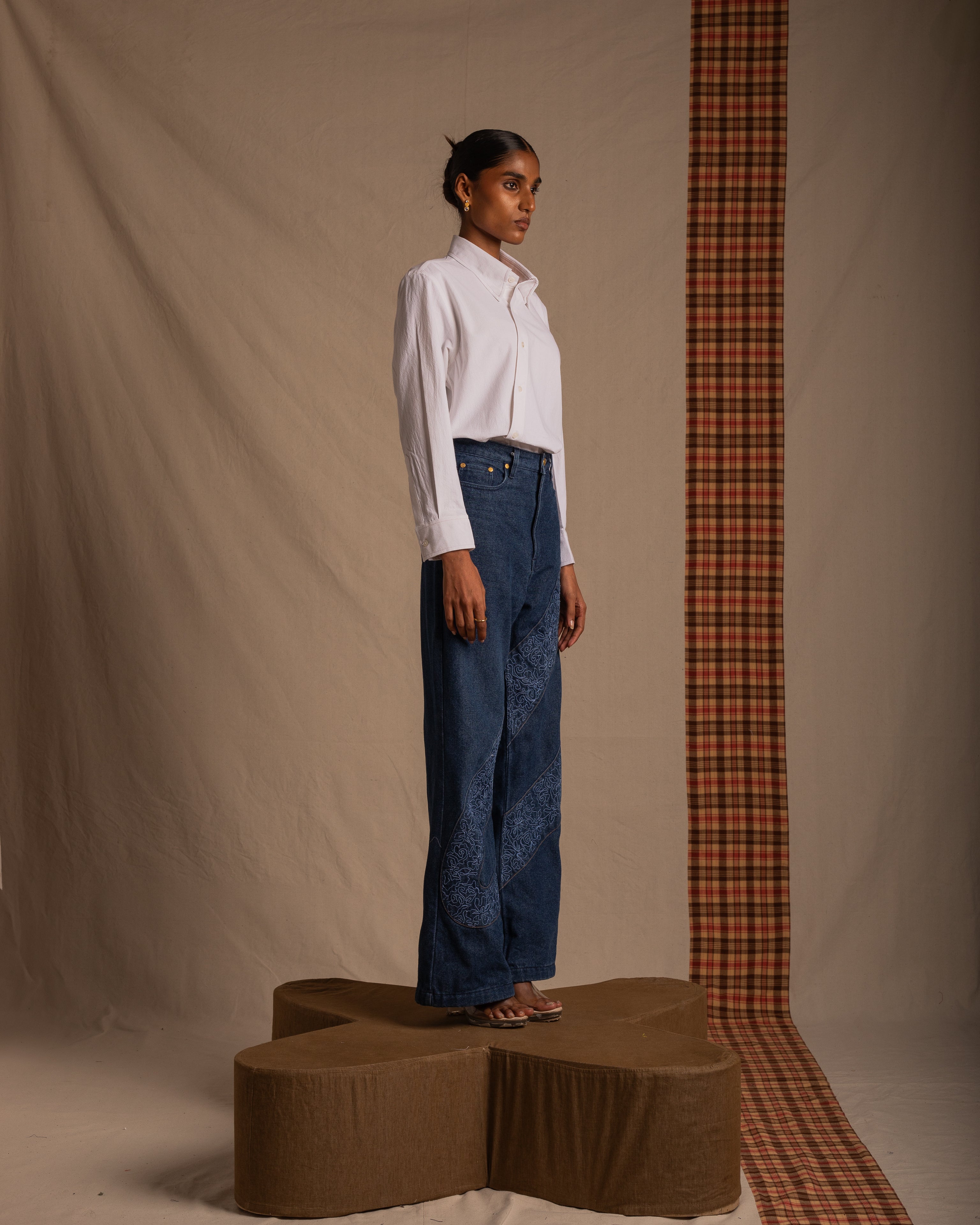 Woman in white button-up shirt and high-waisted embroidered blue jeans standing on a platform, minimal streetwear fashion photo