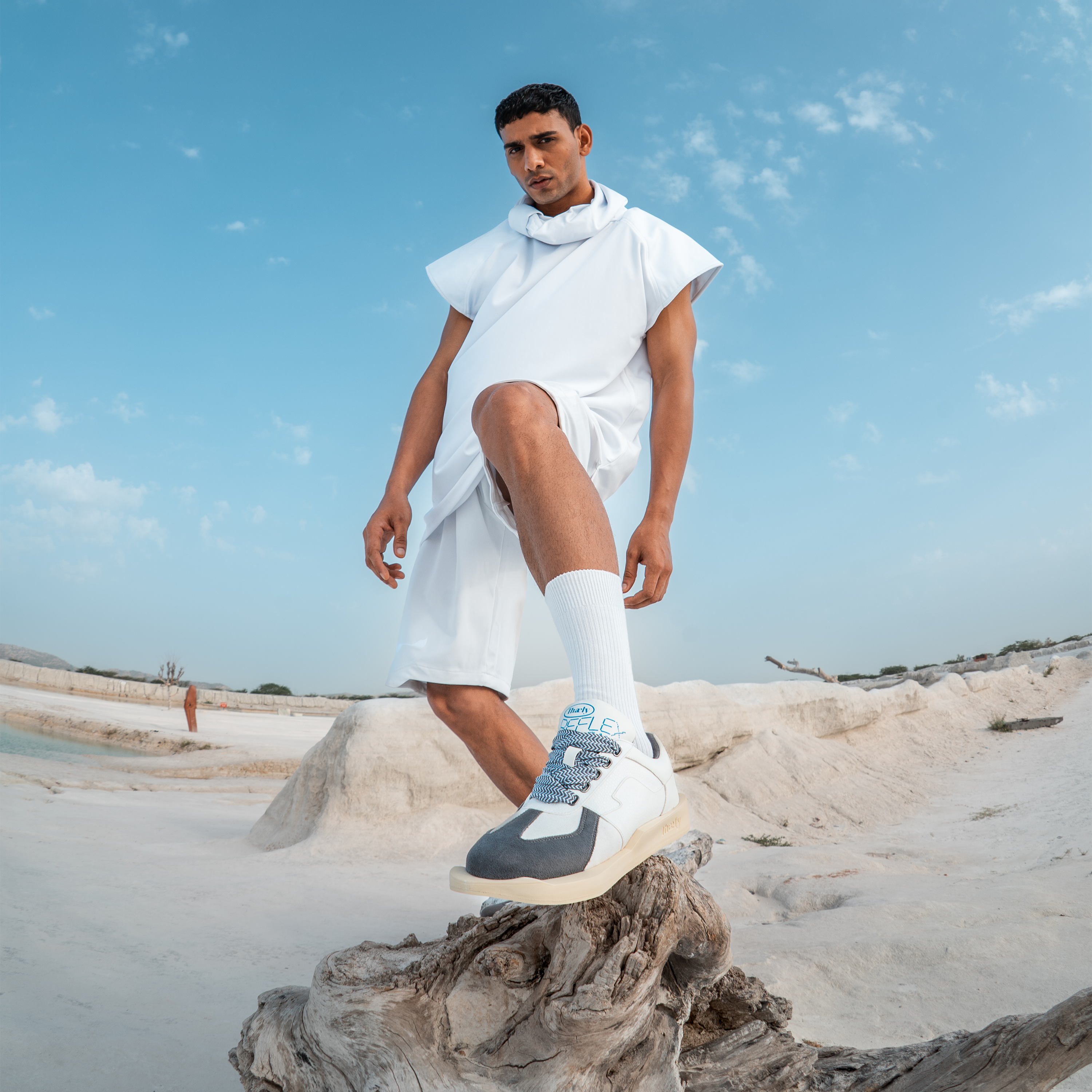 Man in modern streetwear, white hoodie, shorts, and sneakers posing on desert landscape
