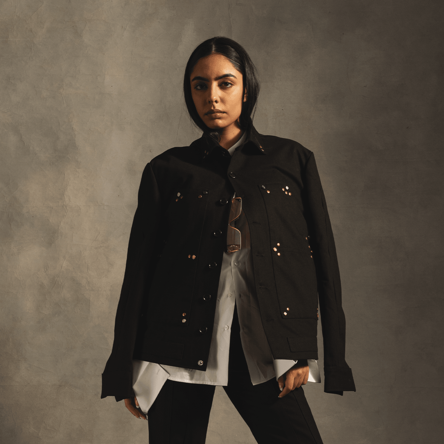 Woman in a black panel jacket with metallic studs, layered over white shirt, streetwear style