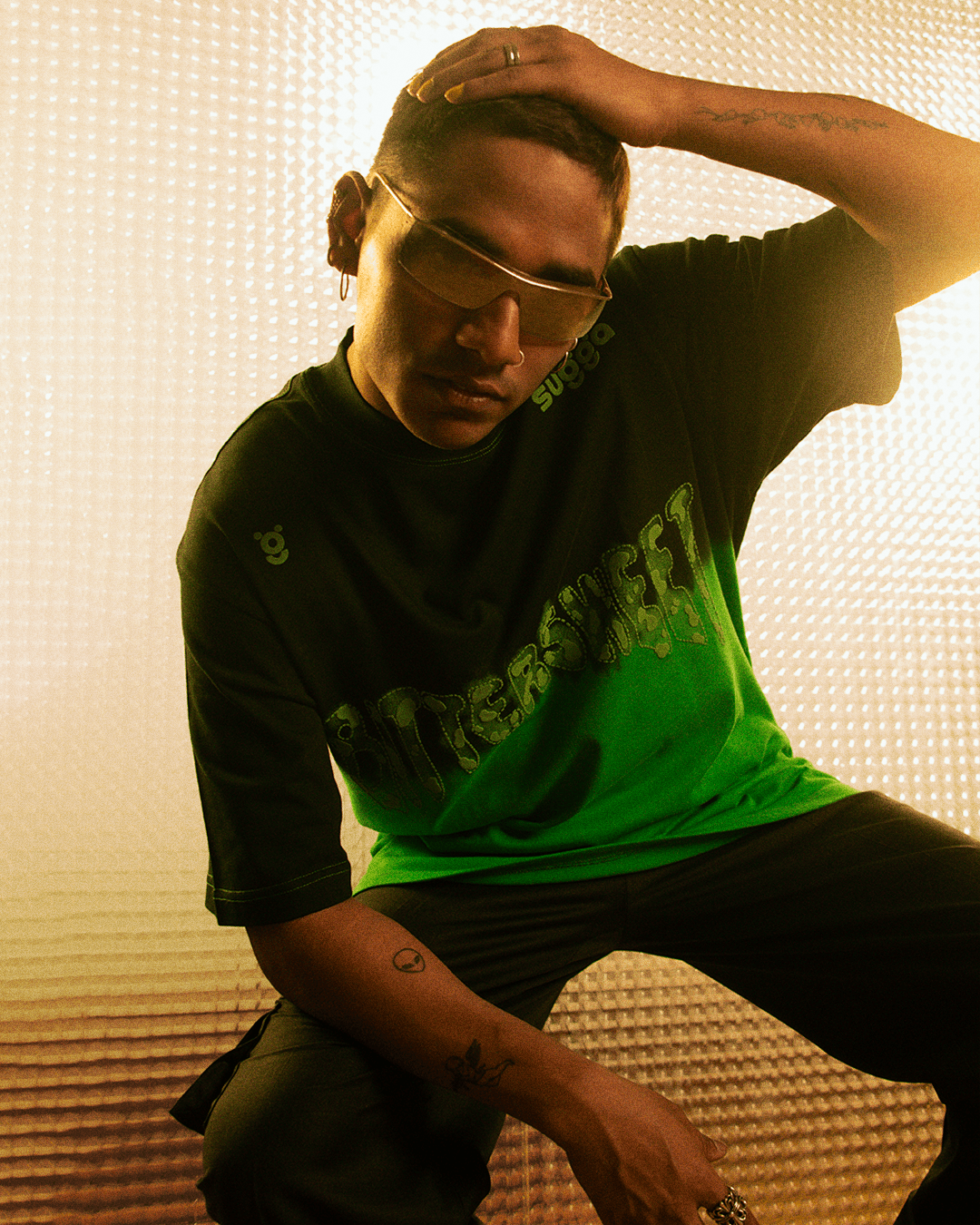 Man in sunglasses wearing green 'bittersweet' graphic streetwear t-shirt with tattoos
