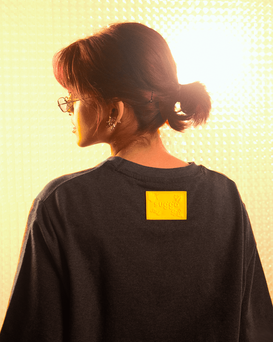 Woman in streetwear black t-shirt with yellow patch, earrings, and sunglasses, back view