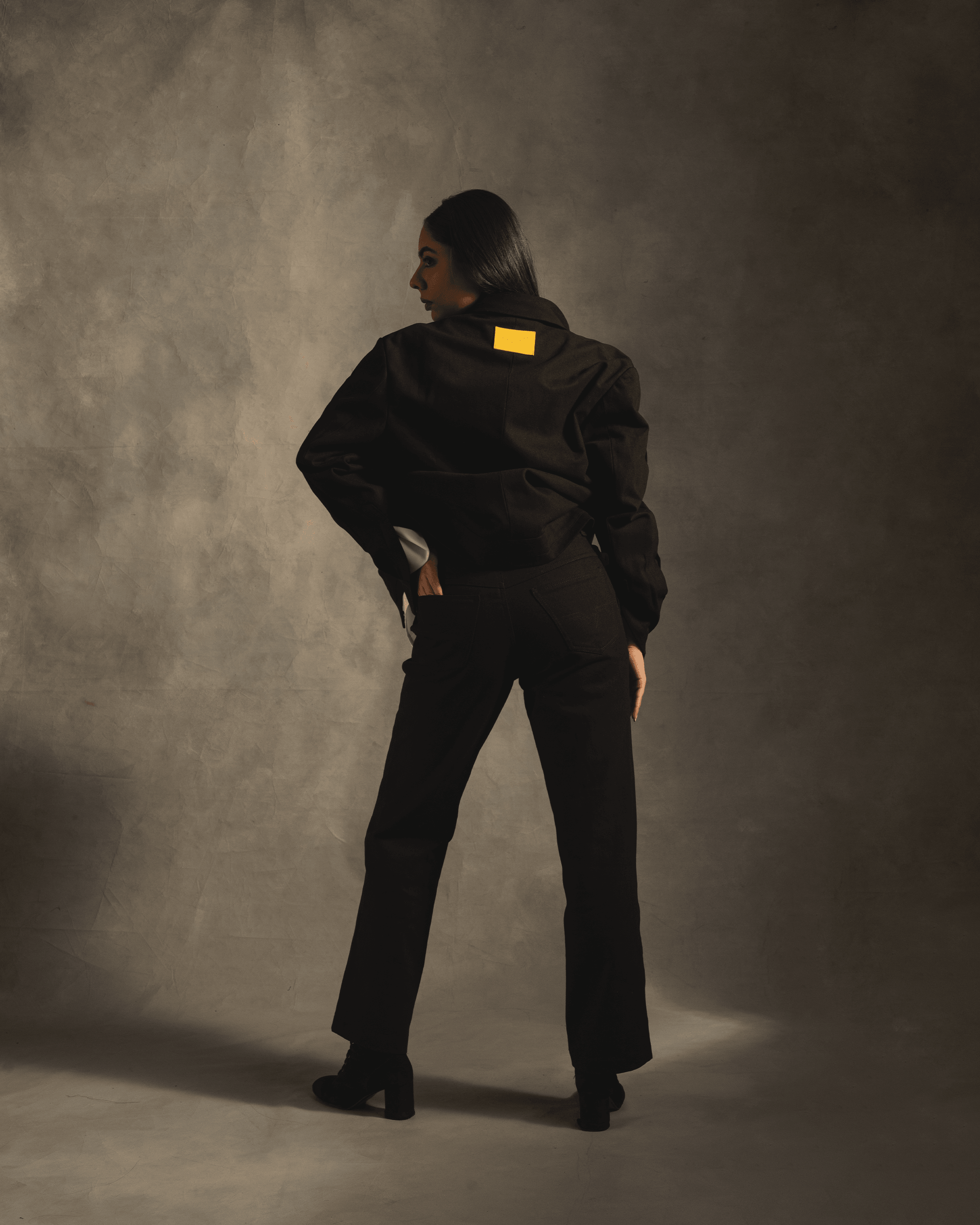 Woman modeling black streetwear jacket and pants with a yellow patch on the back