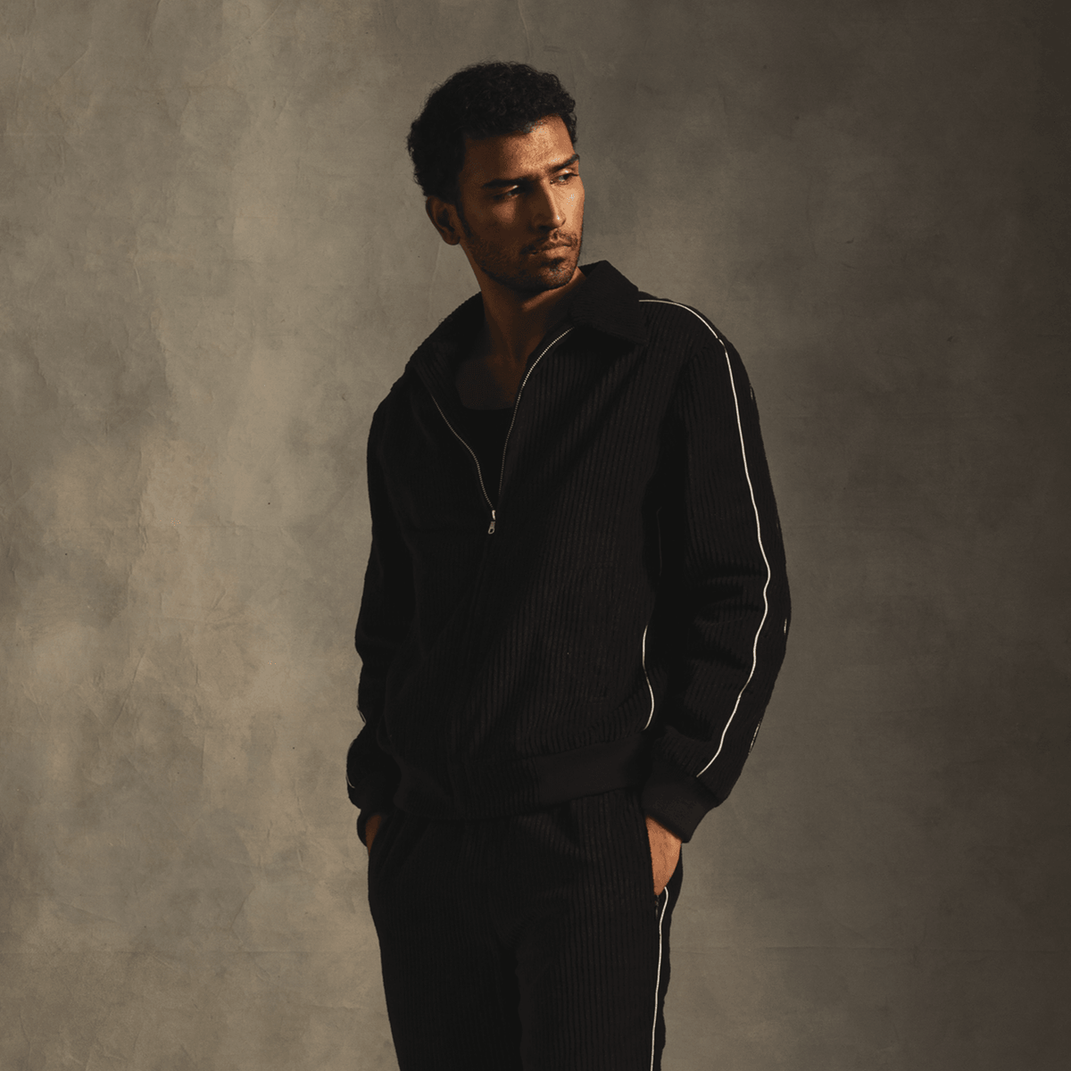 Man modeling black streetwear tracksuit with white piping in studio setting
