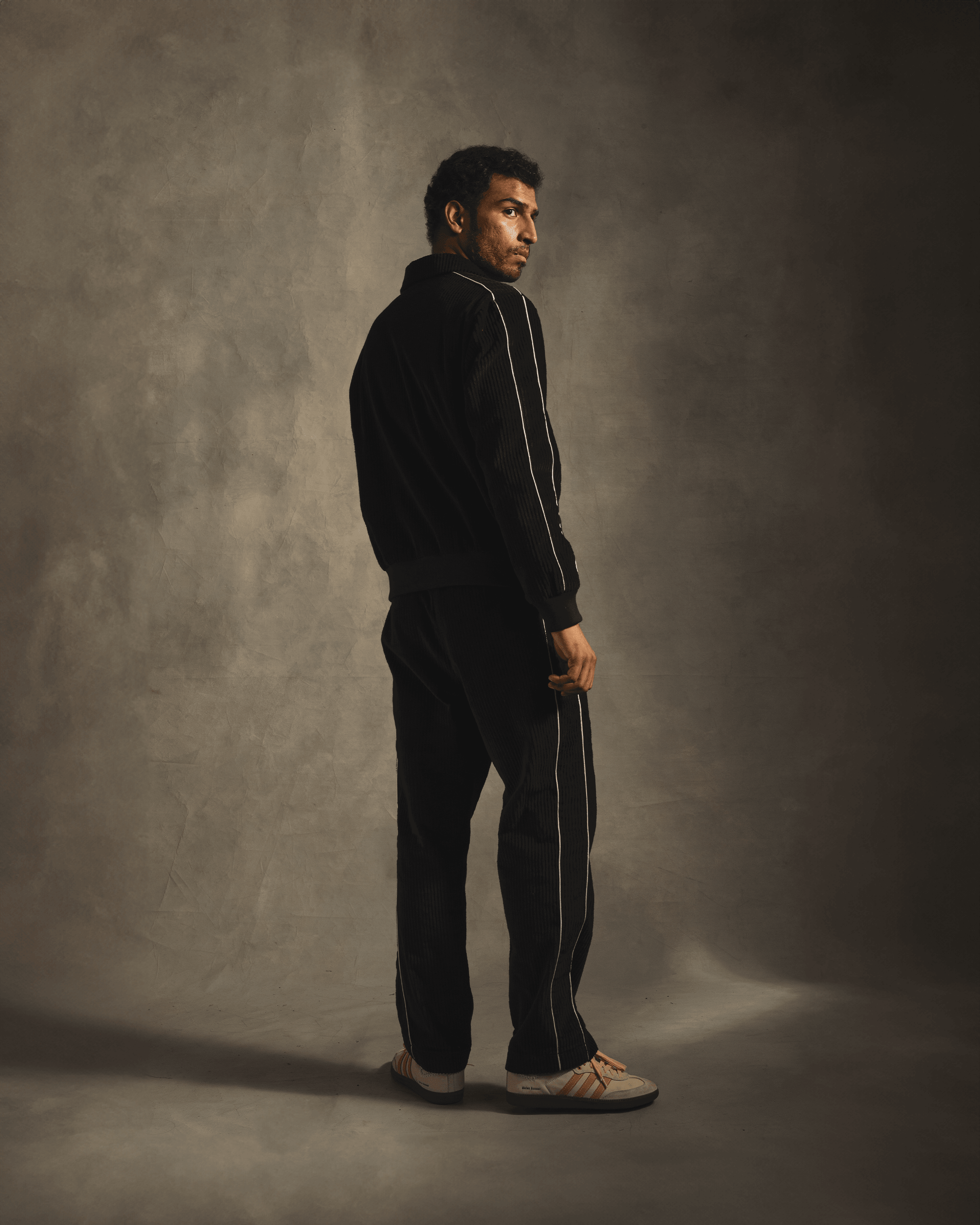 Man wearing black corduroy streetwear tracksuit with white piping and sneakers