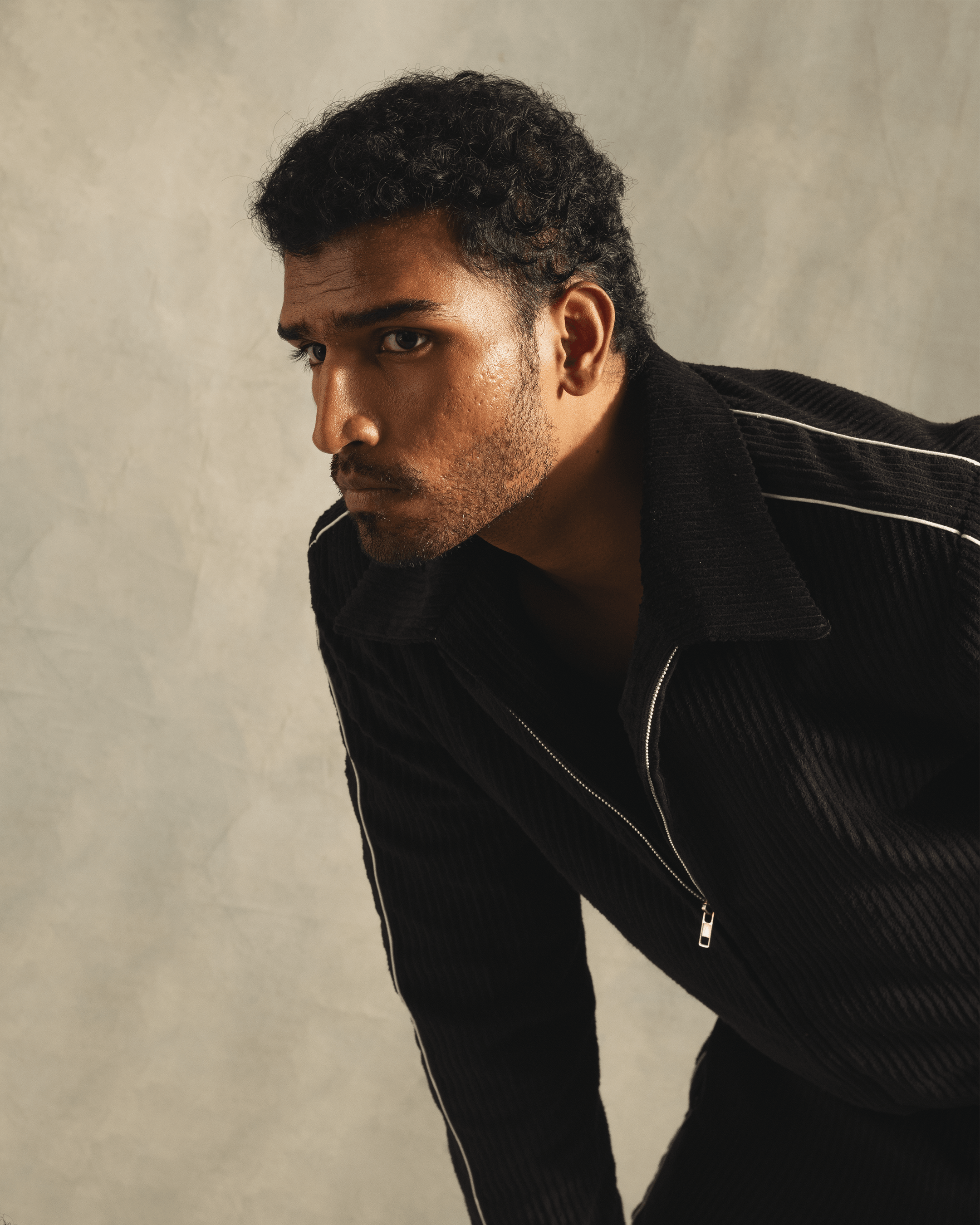 Man in a black zip-up jacket with white piping, posing against a neutral backdrop, streetwear fashion