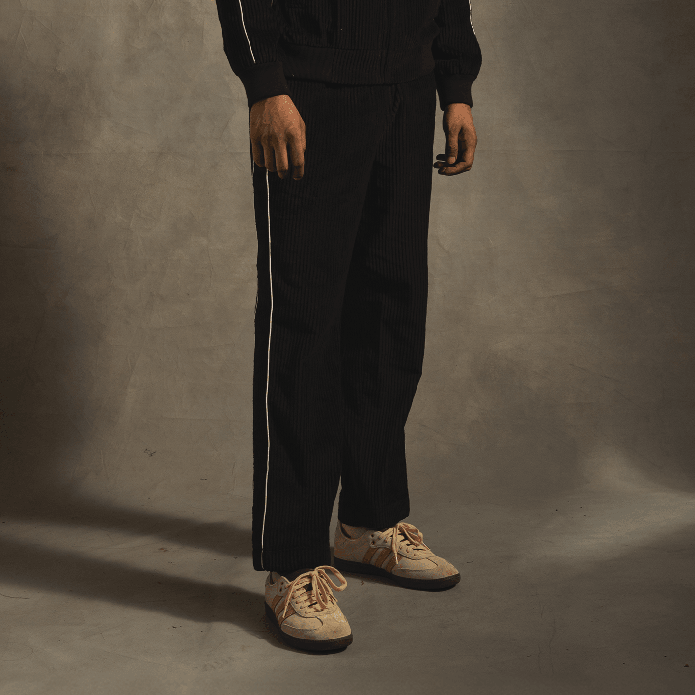 Man wearing black corduroy tracksuit pants with white side stripes and beige sneakers