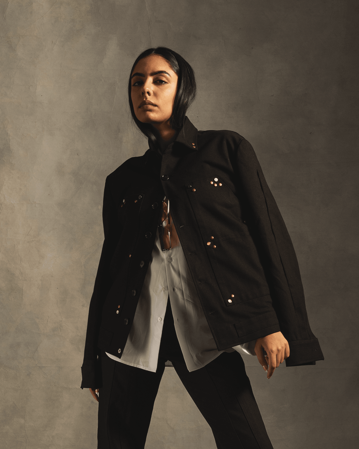 Woman wearing black studded streetwear jacket over white shirt and black pants