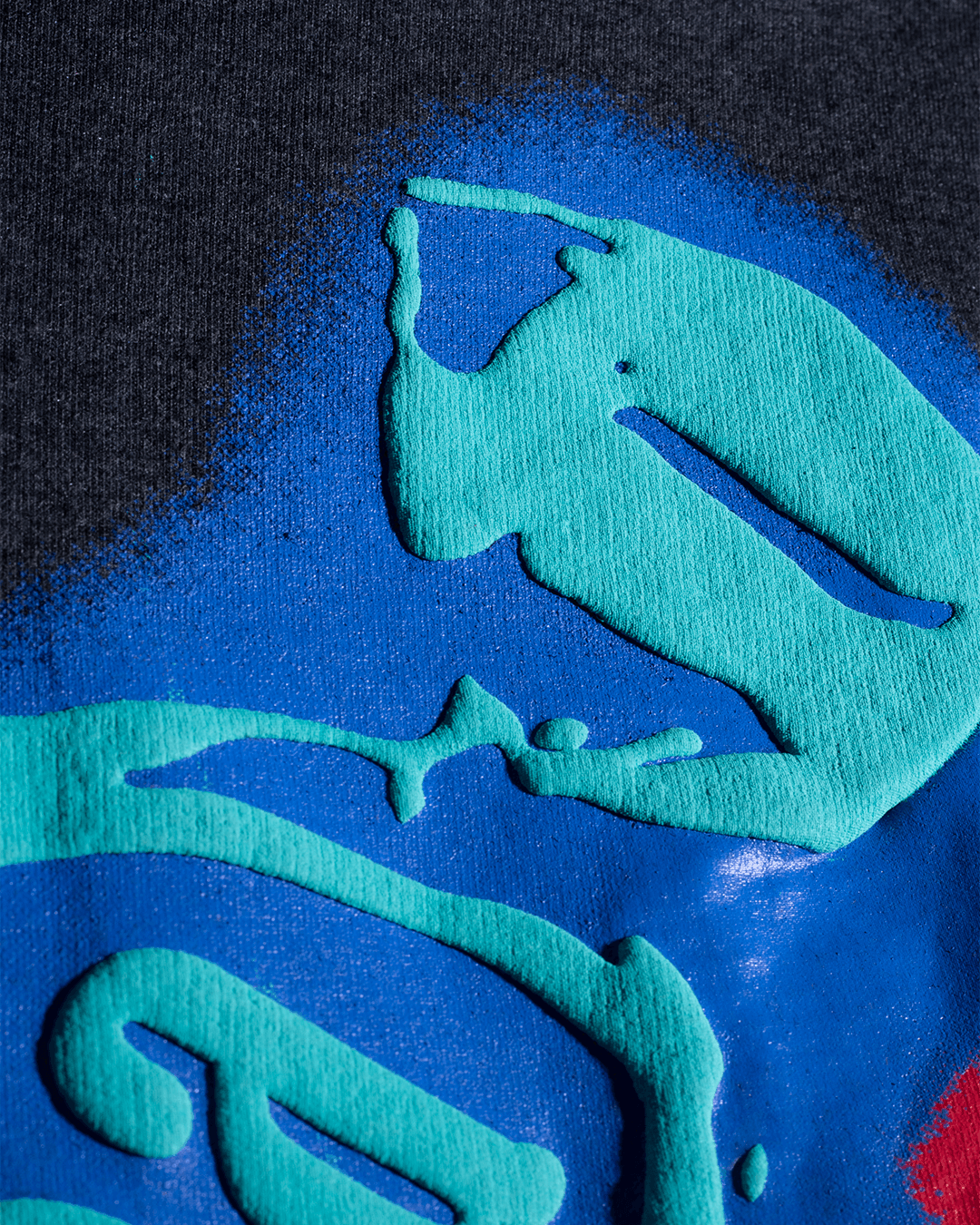 Close-up of streetwear graphic print with raised turquoise and blue textured details on fabric