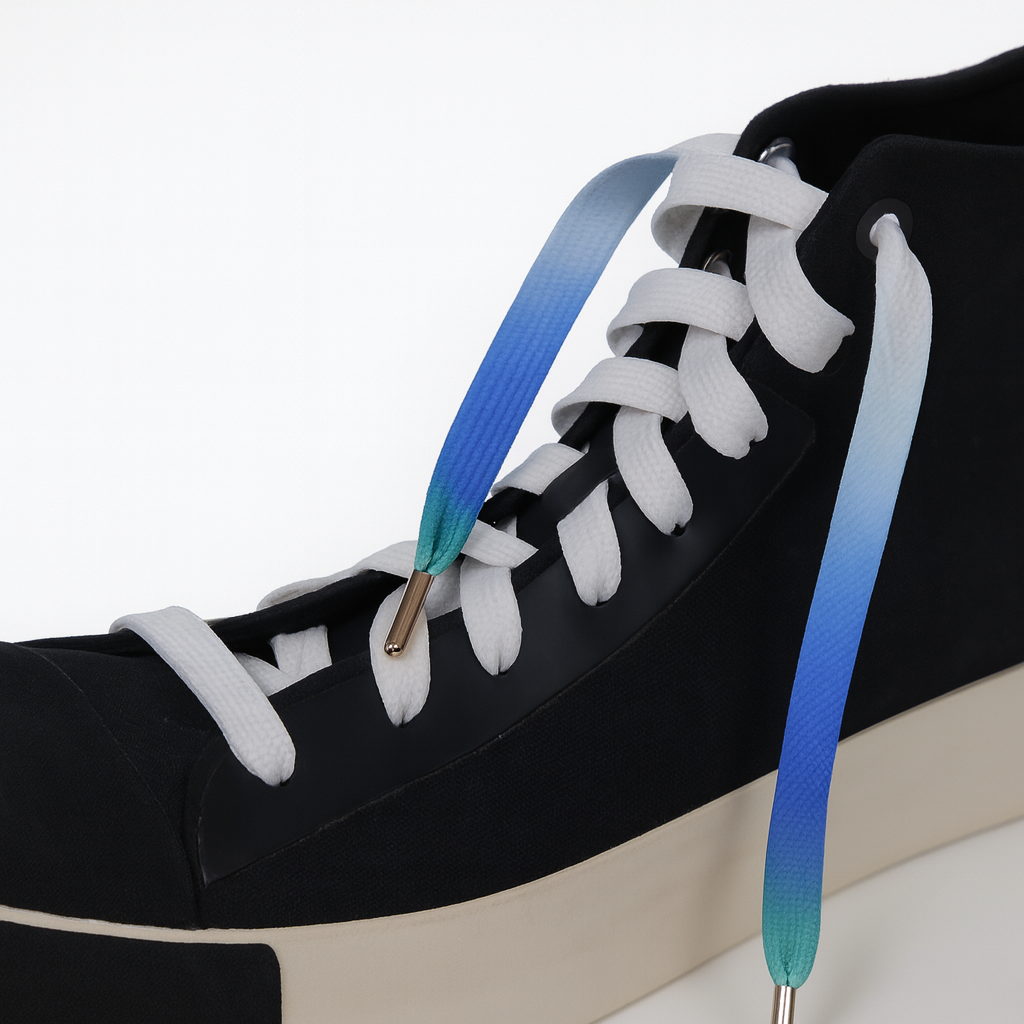 Black sneaker with white laces and a gradient blue to green sole on a white background
