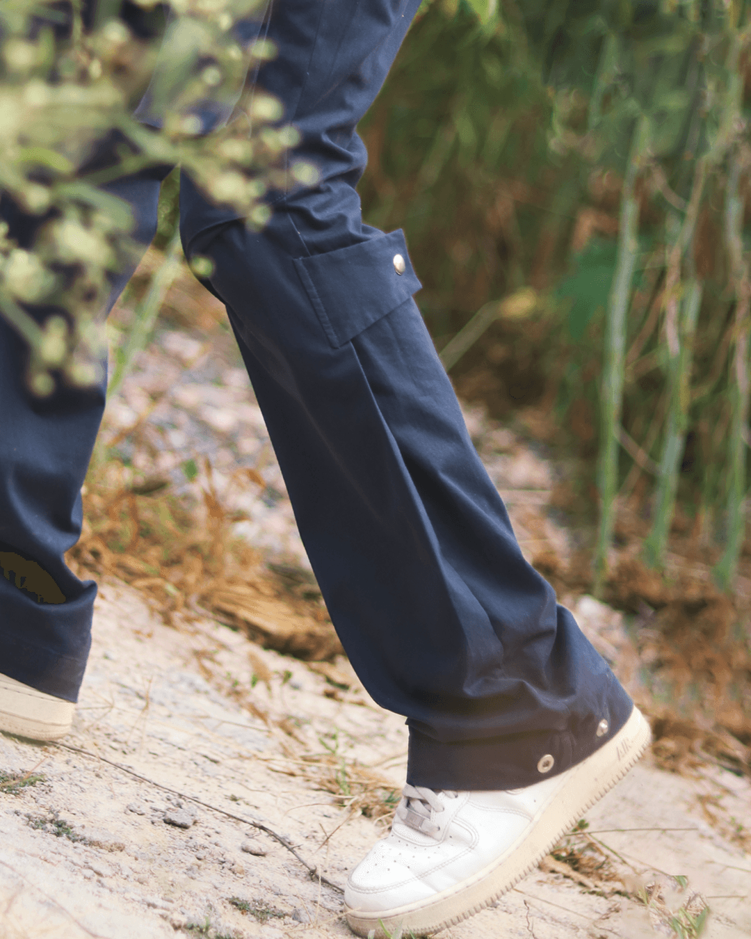 Blue cargo pants with side pocket and snap details, styled with white sneakers outdoors