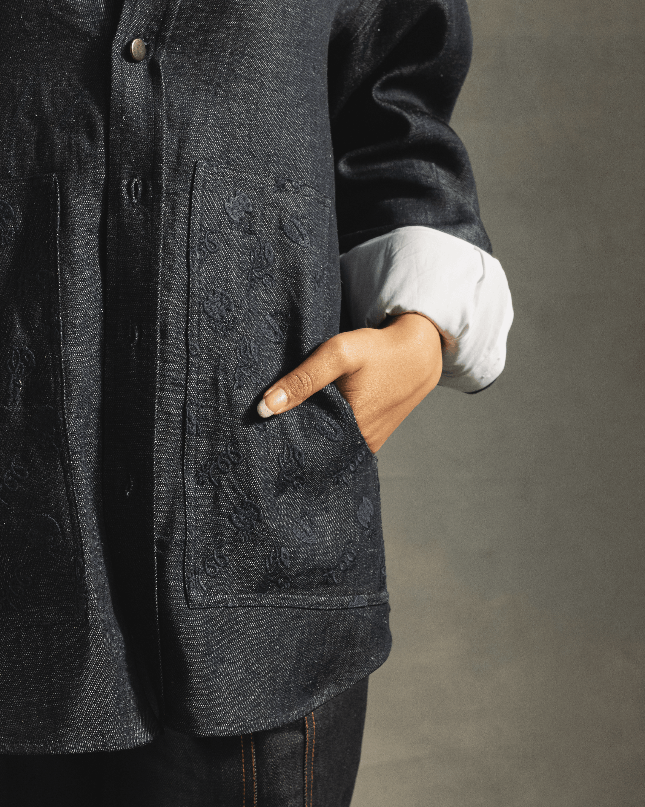 Close-up of a person wearing a dark blue denim shirt with embossed patch pockets and white cuff detail