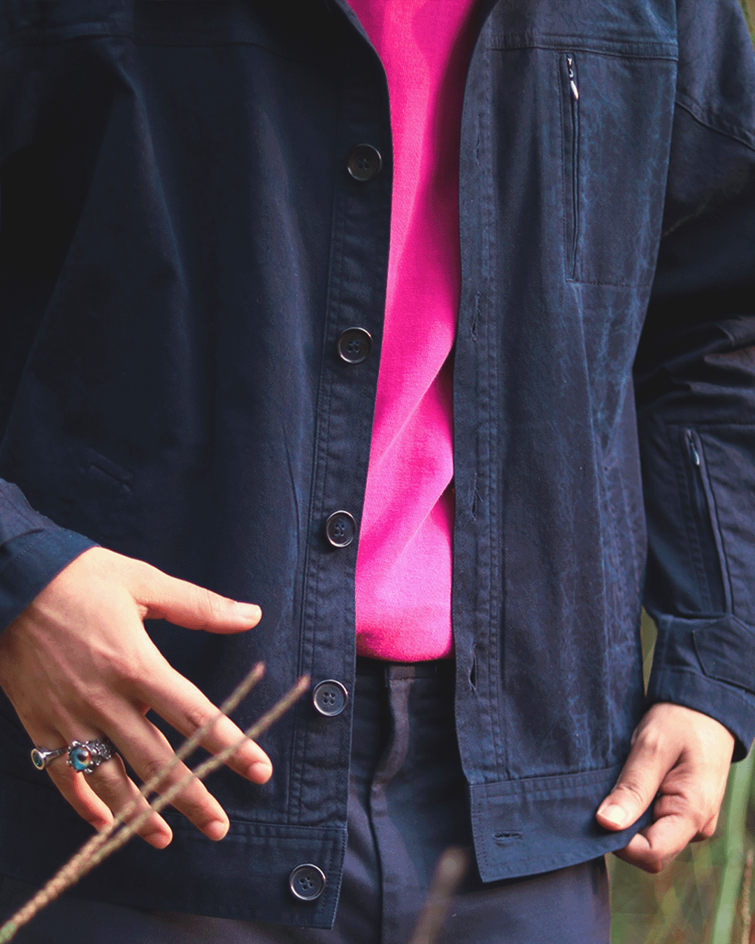 Man wearing a navy blue streetwear jacket over a pink shirt, stylish rings on hand