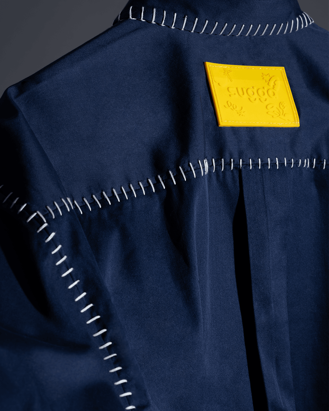 Close-up of blue streetwear shirt with white contrast stitching and yellow embossed patch