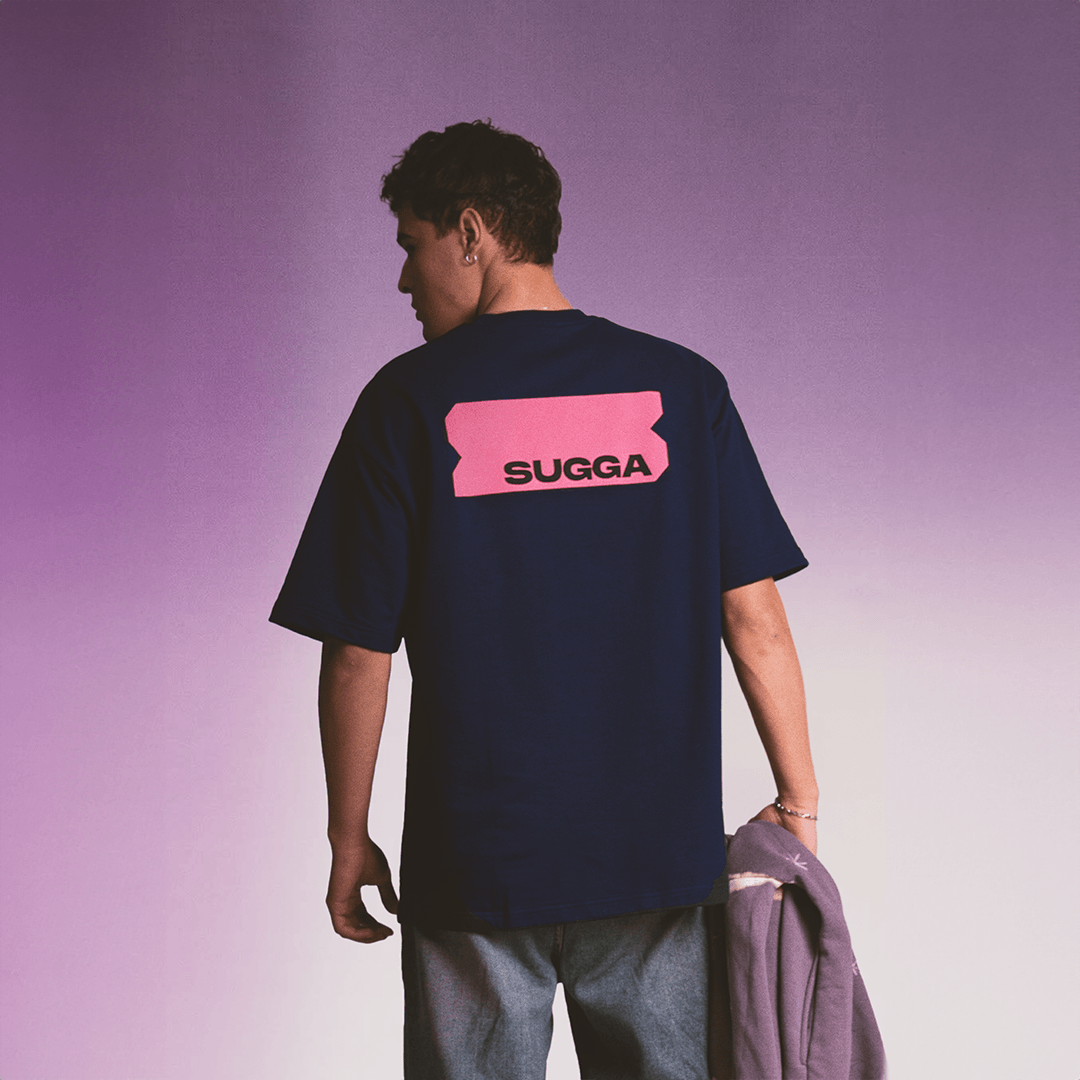 Man wearing navy streetwear t-shirt with pink SUGGA graphic on back, purple gradient background