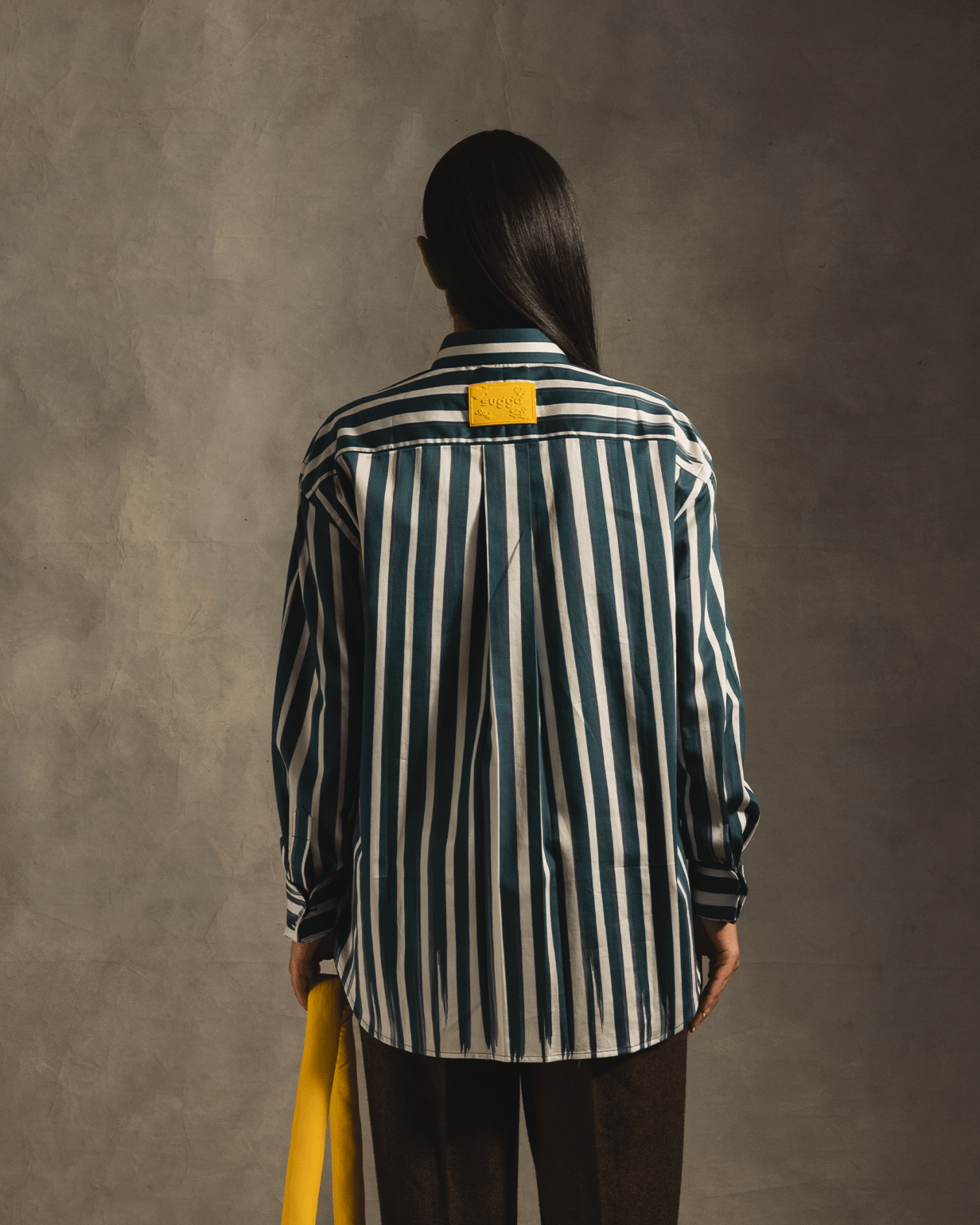 Person wearing blue and white vertical striped streetwear shirt with yellow tag, back view