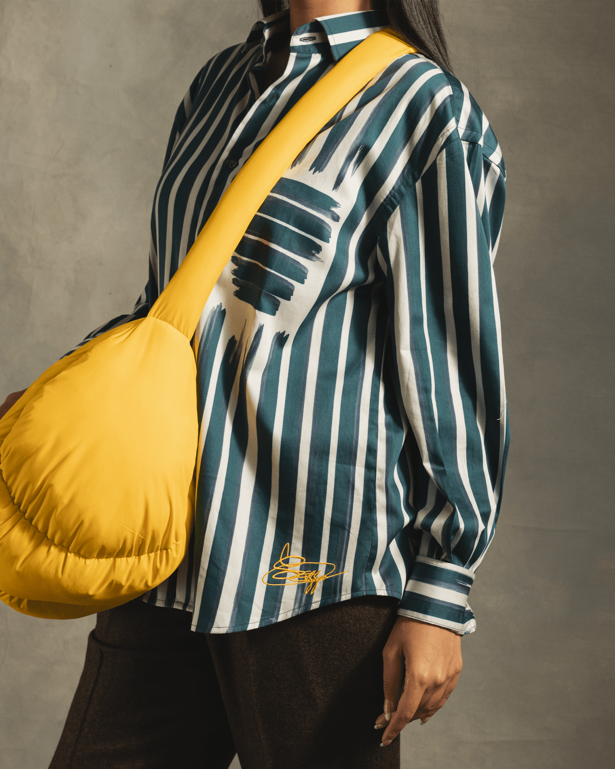 Person wearing a blue and white striped streetwear shirt with yellow graphic detail and carrying a large yellow puffer shoulder bag.
