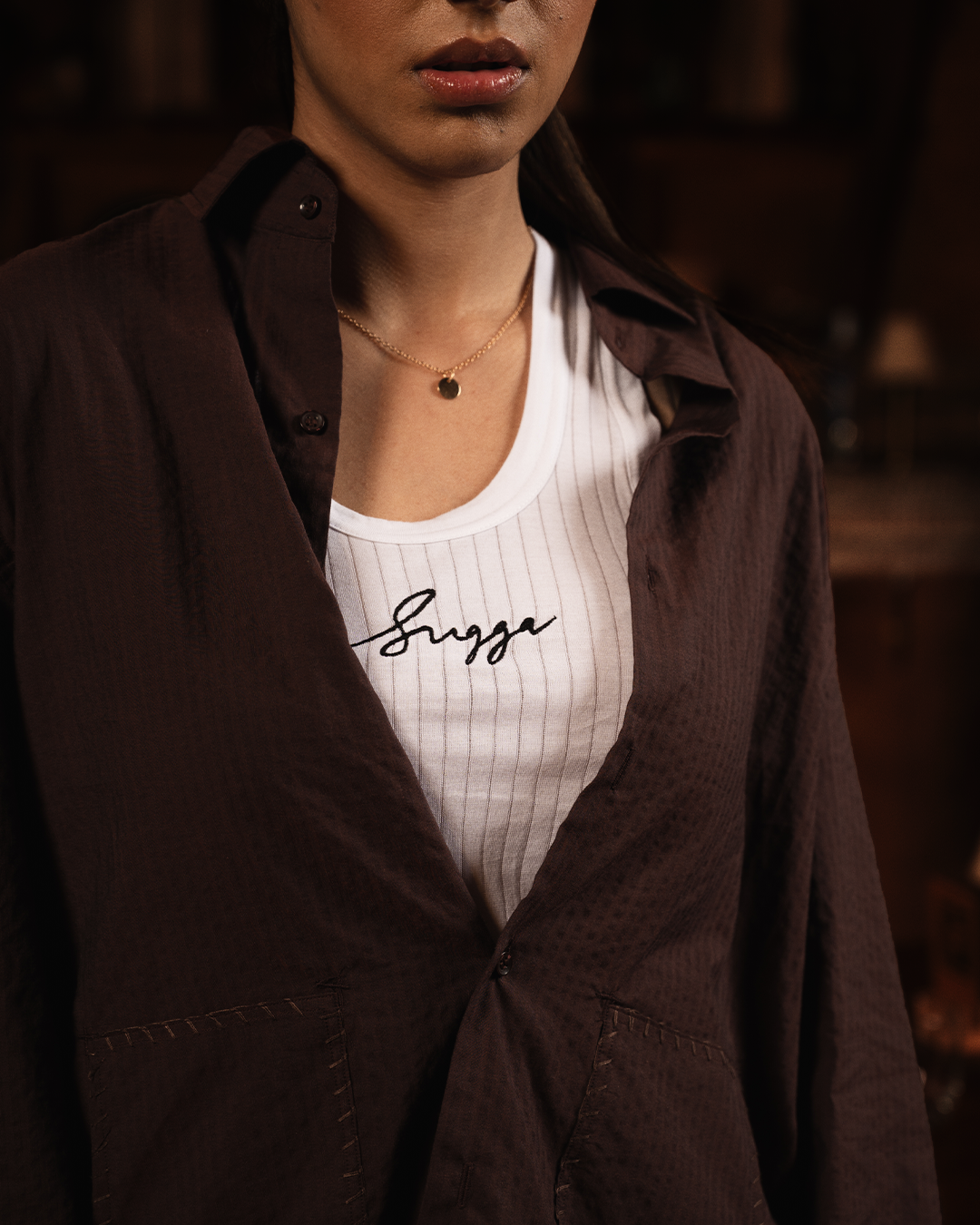 Woman wearing a brown textured button-up shirt over a white ribbed tank top with lettering, streetwear style.
