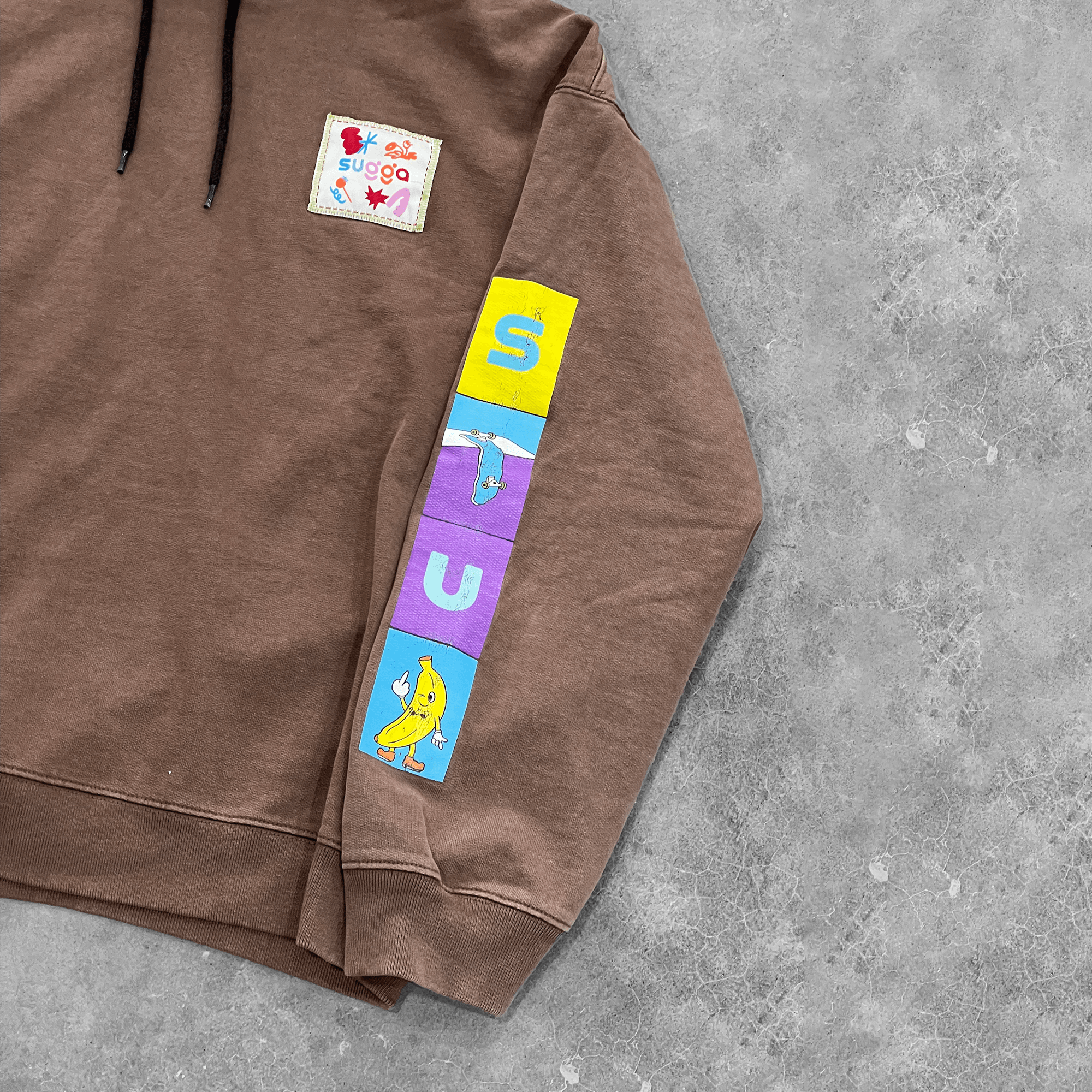 Brown streetwear hoodie with colorful cartoon sleeve graphics and patch on chest