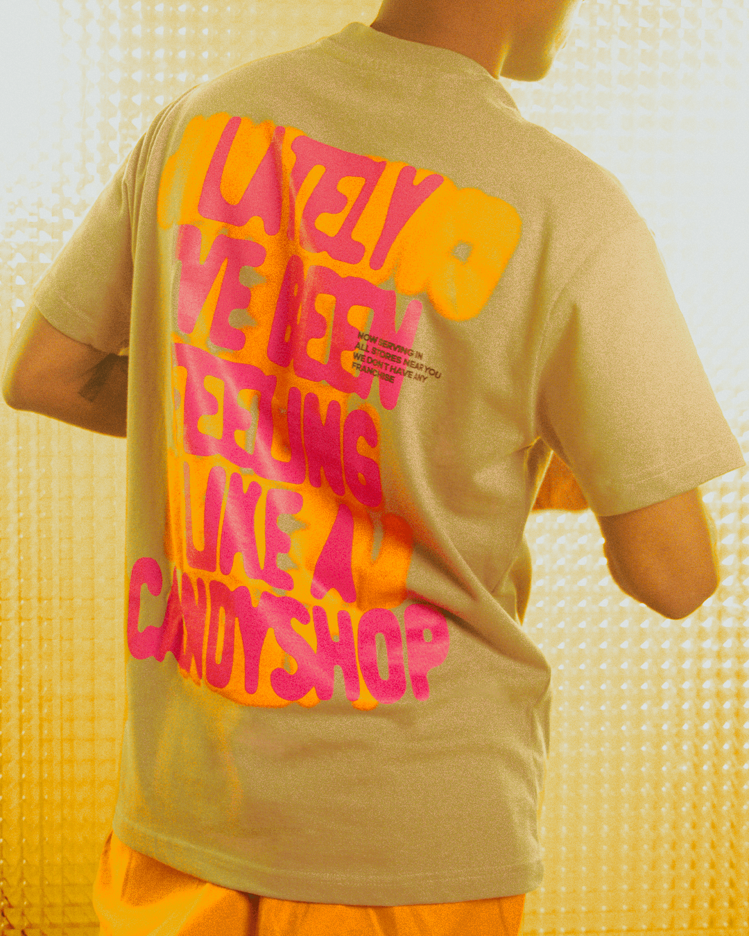 Man wearing beige streetwear t-shirt with bold neon orange and pink graphic text on back