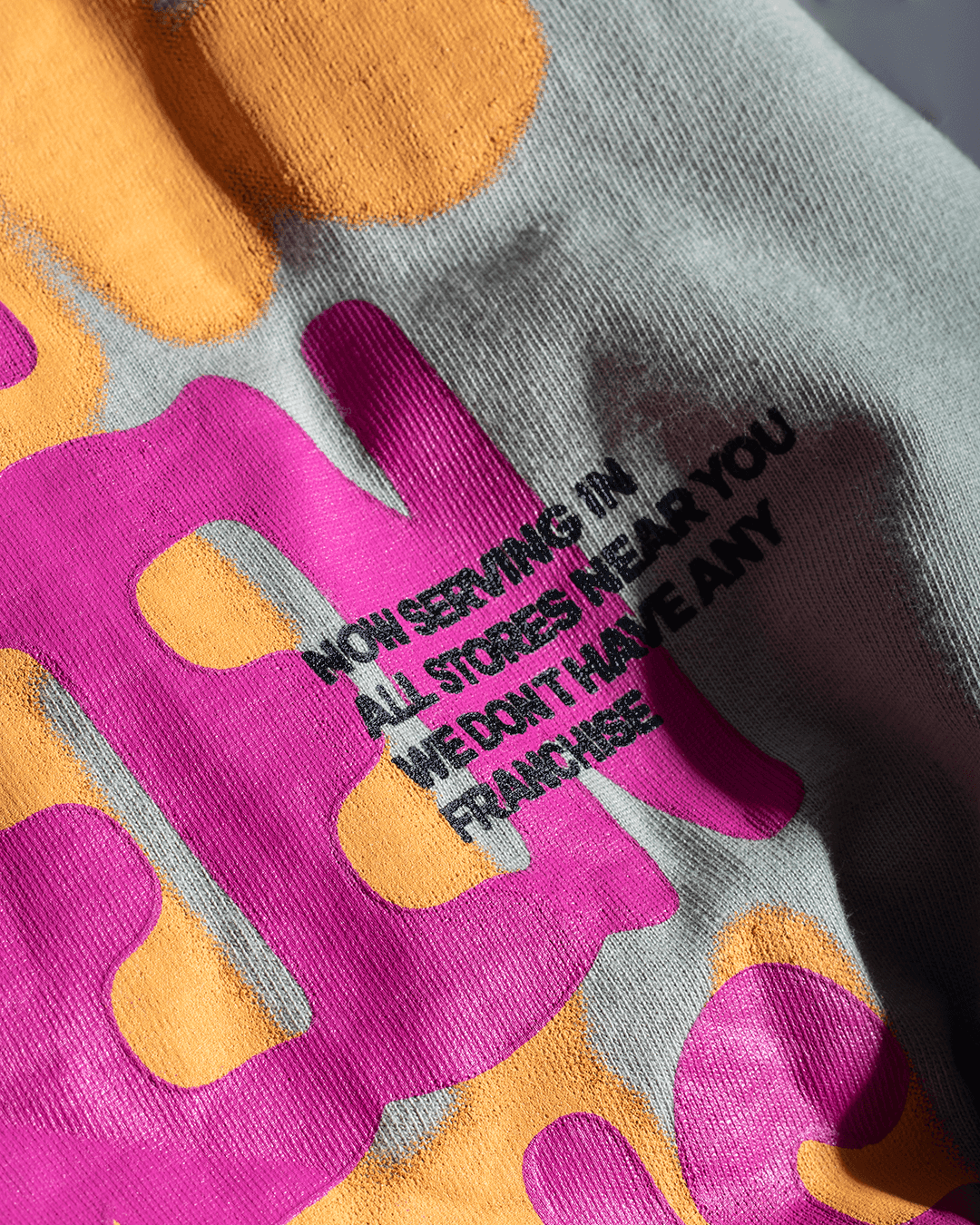 Close-up of streetwear graphic shirt with bold pink and orange lettering and printed text detail