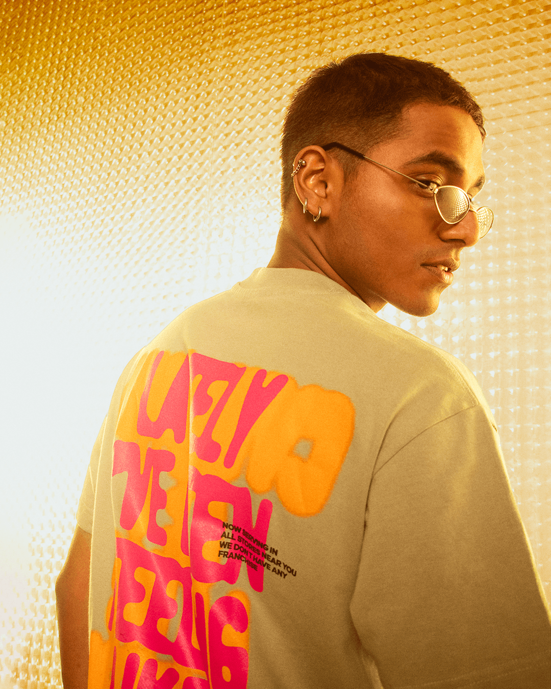 Man wearing streetwear t-shirt with bold neon graphic, posing in a modern, golden-lit setting.