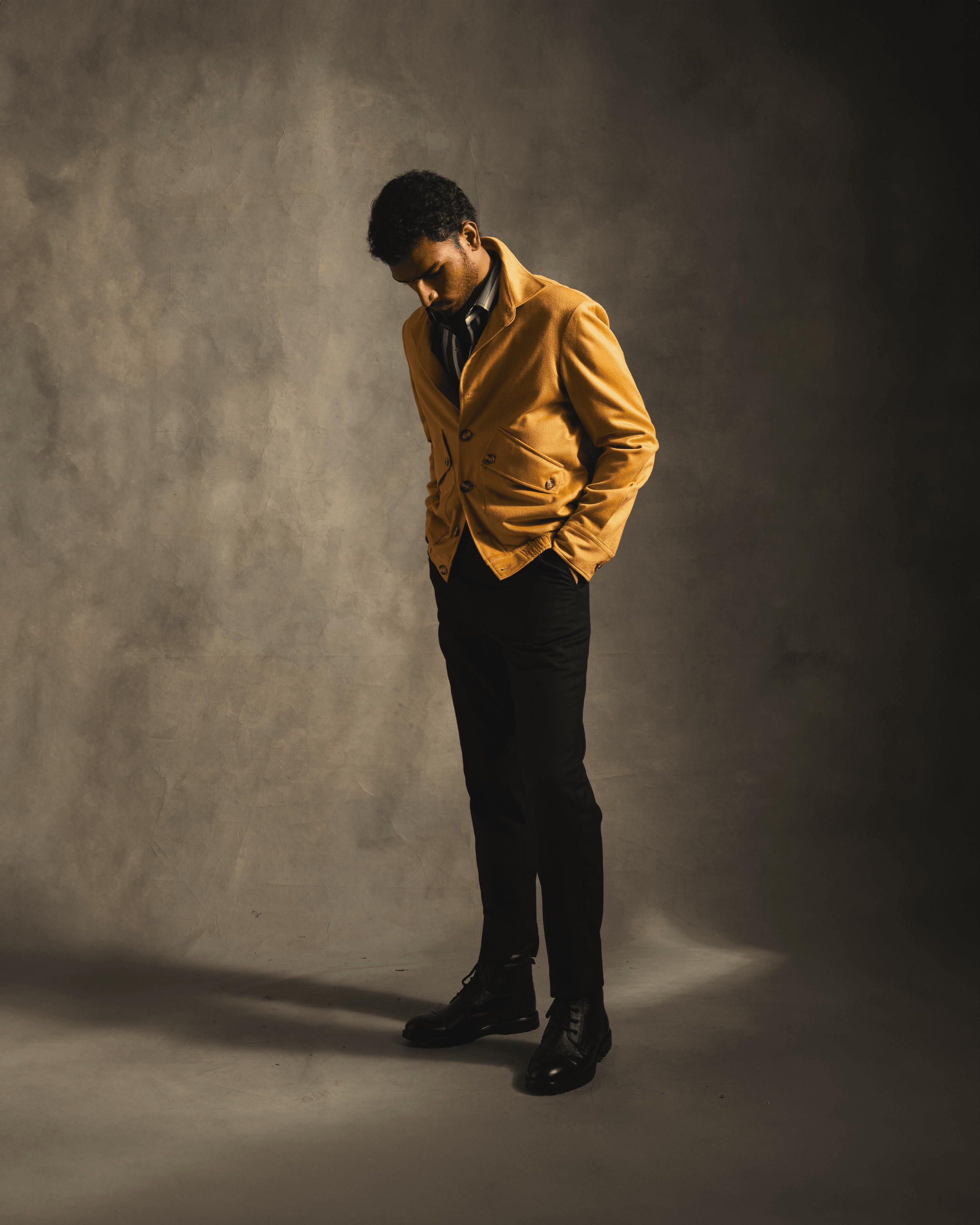 Man wearing camel cashmere bomber jacket, black pants, and boots in studio lighting