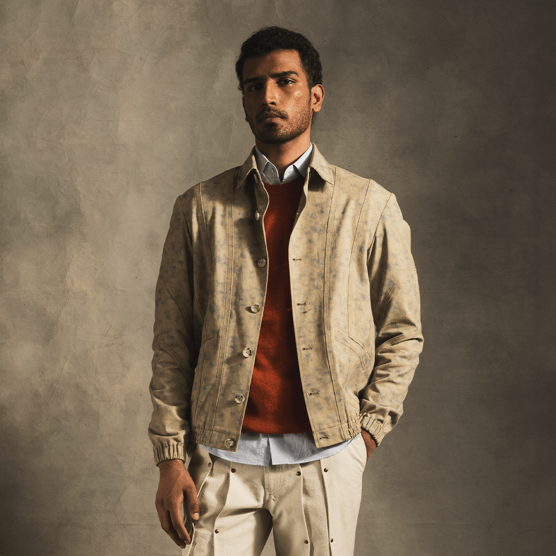 Man modeling modern streetwear with beige patterned jacket, red sweater, and light trousers