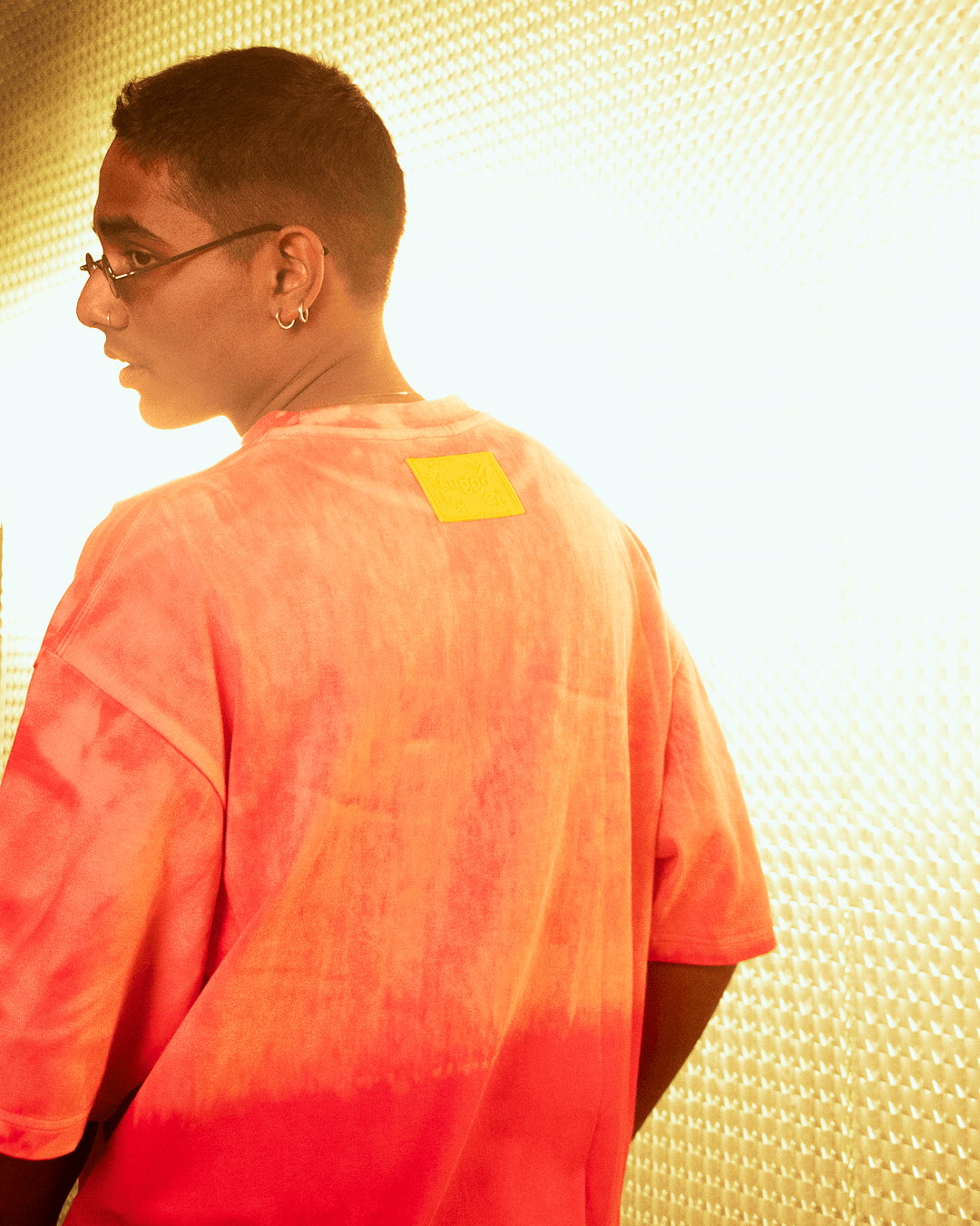 Man wearing oversized orange tie-dye streetwear t-shirt with patch detail, stylish lighting