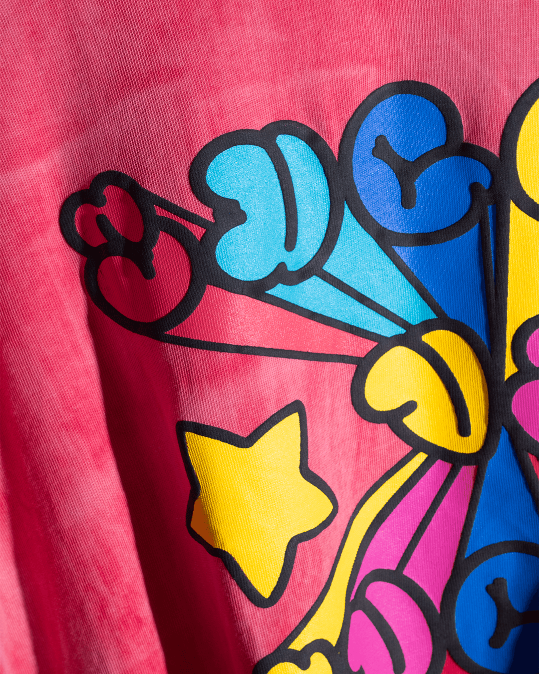 Close-up of vibrant graphic print with blue, yellow, and pink shapes on a red streetwear shirt