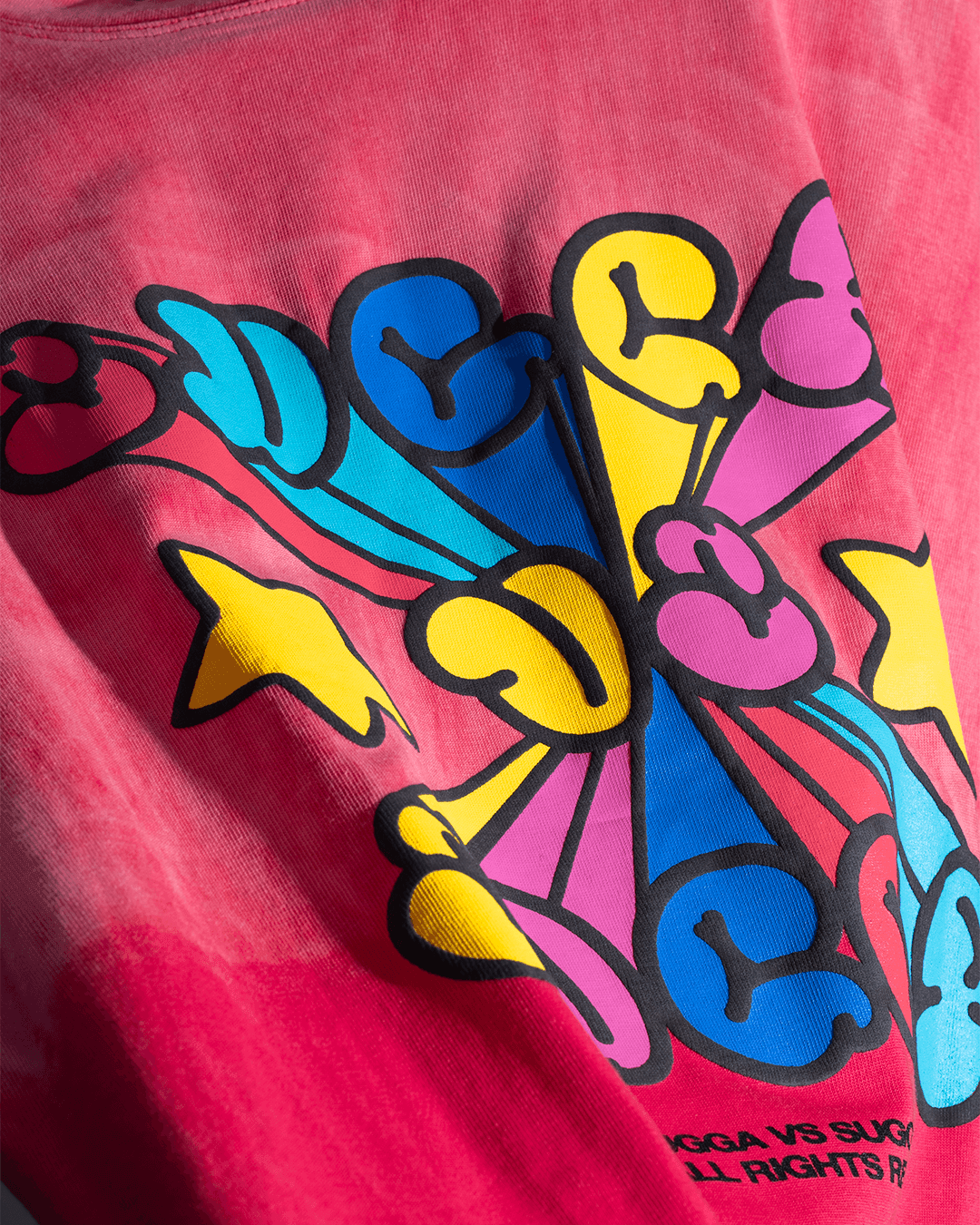 Close-up of a pink streetwear t-shirt with colorful abstract graphic print, vibrant yellow, blue, and pink design details.