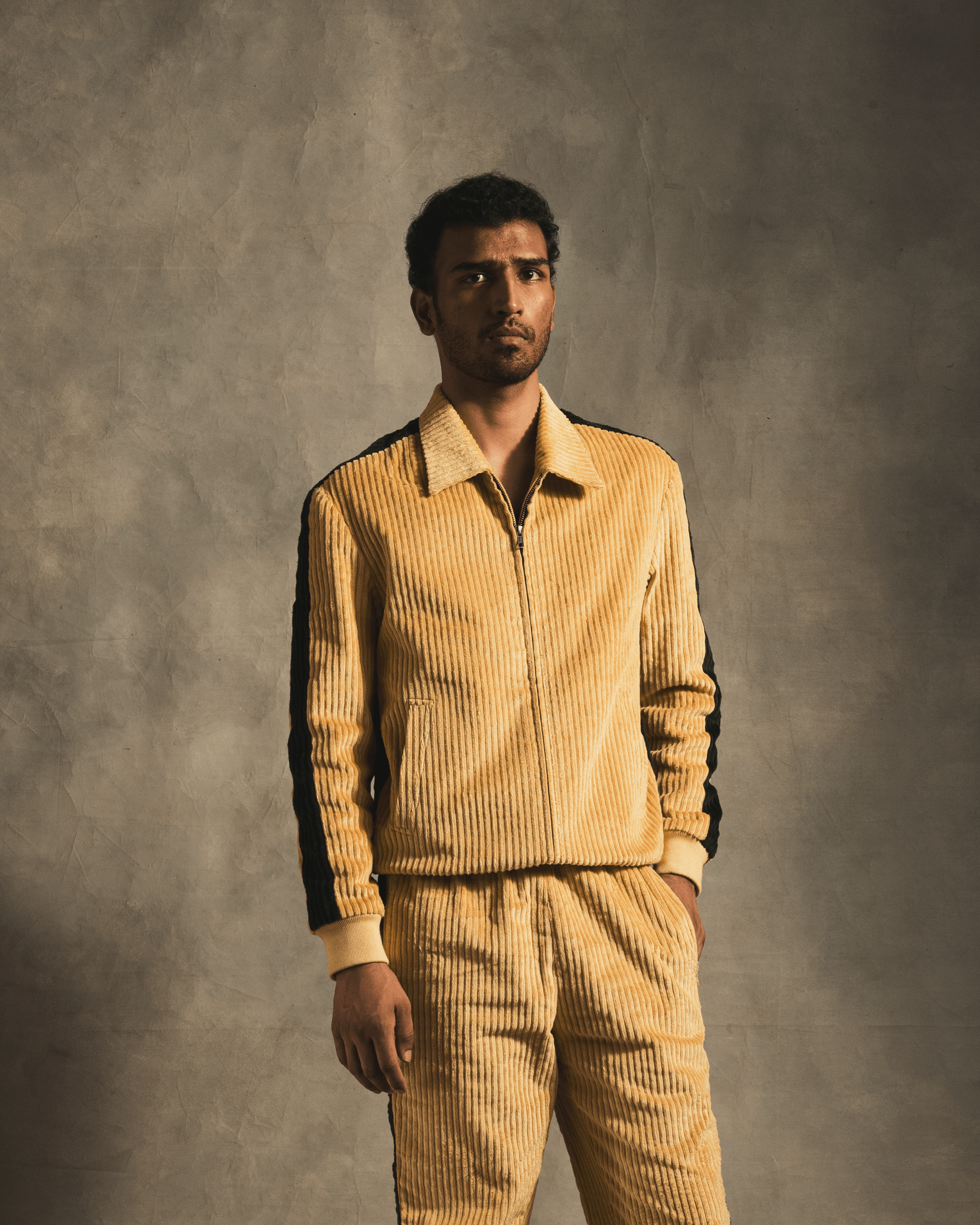 Man wearing a cream corduroy track jacket and matching pants with black stripe details