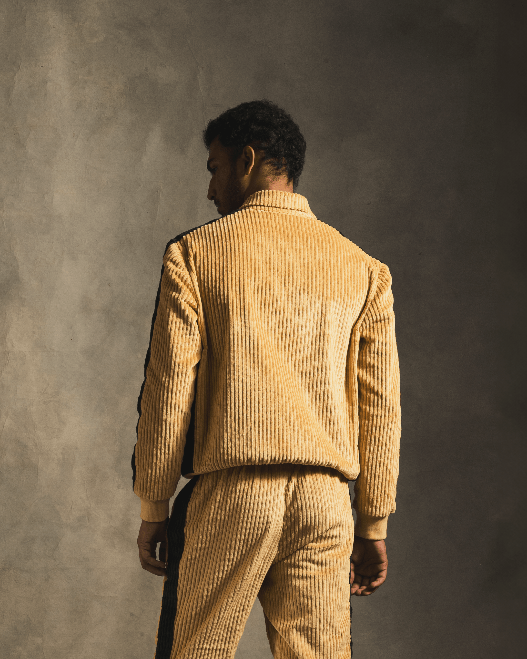 Man wearing ribbed cream track jacket and pants set with black side stripes, back view