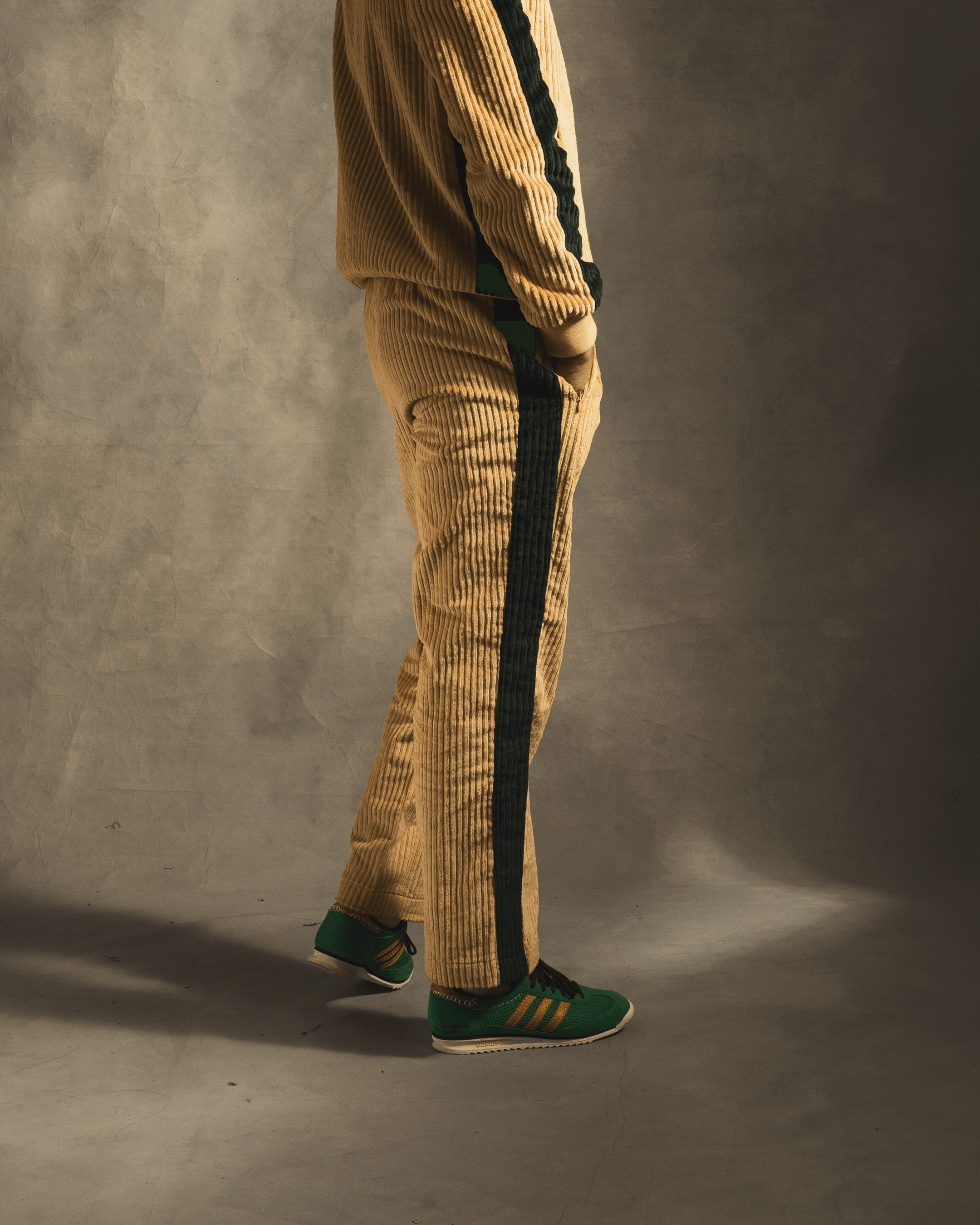 Cream corduroy track pants with black side stripes styled with green and yellow sneakers
