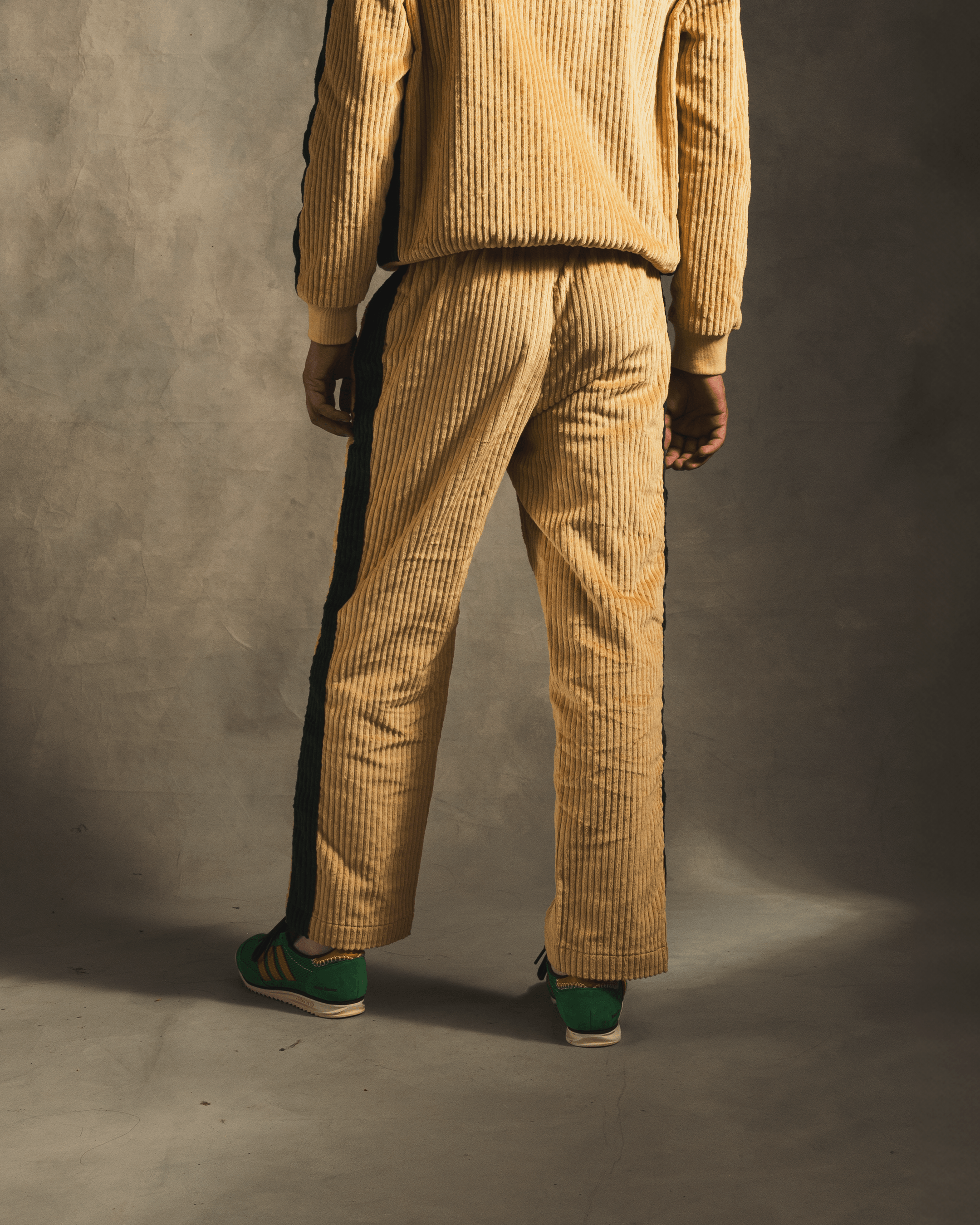 Back view of cream corduroy track pants with black side stripe, styled with green sneakers