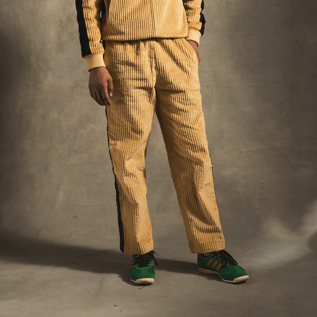 Cream corduroy track pants with black side stripes, styled with green sneakers