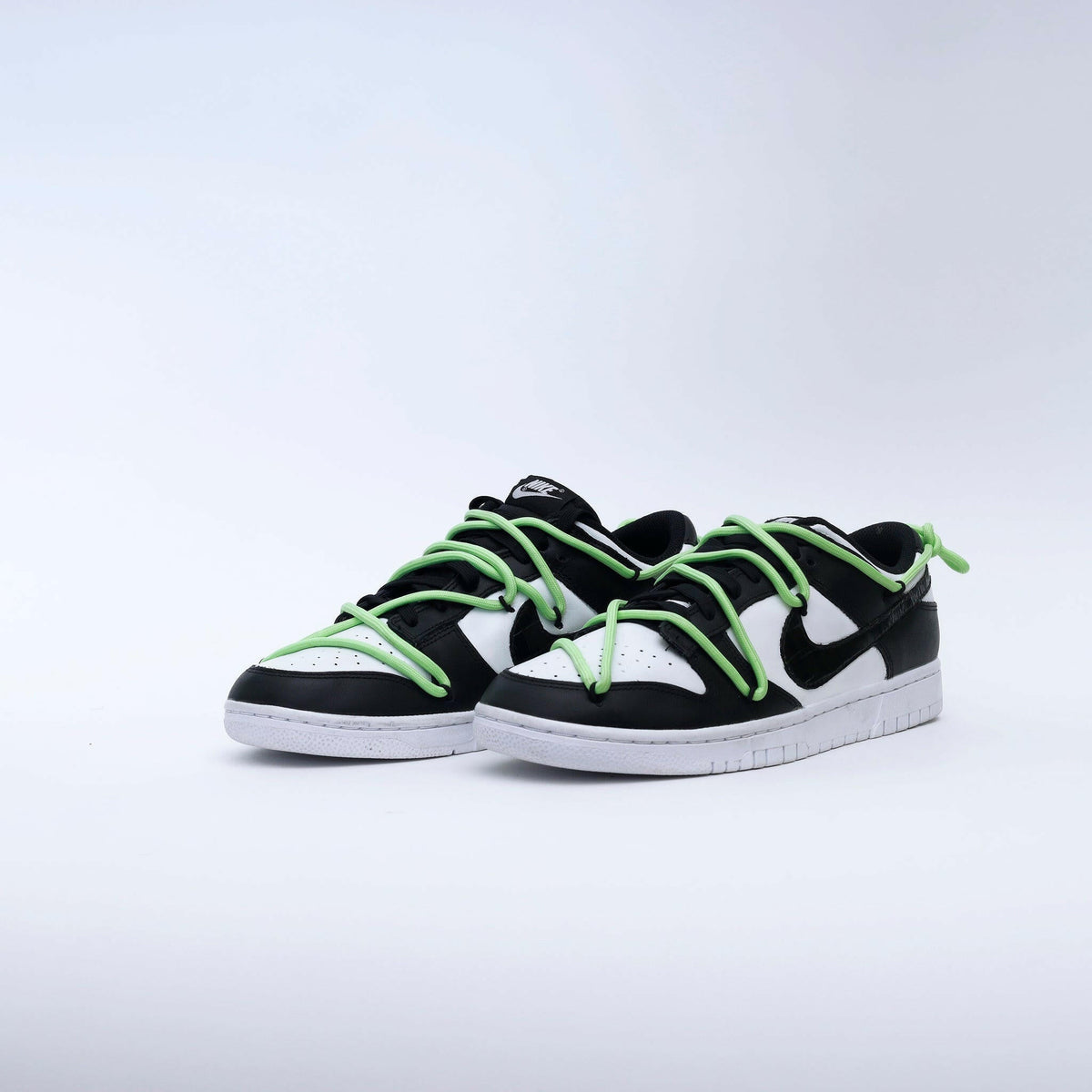 Black and white low-top streetwear sneakers with neon green laces on a white background