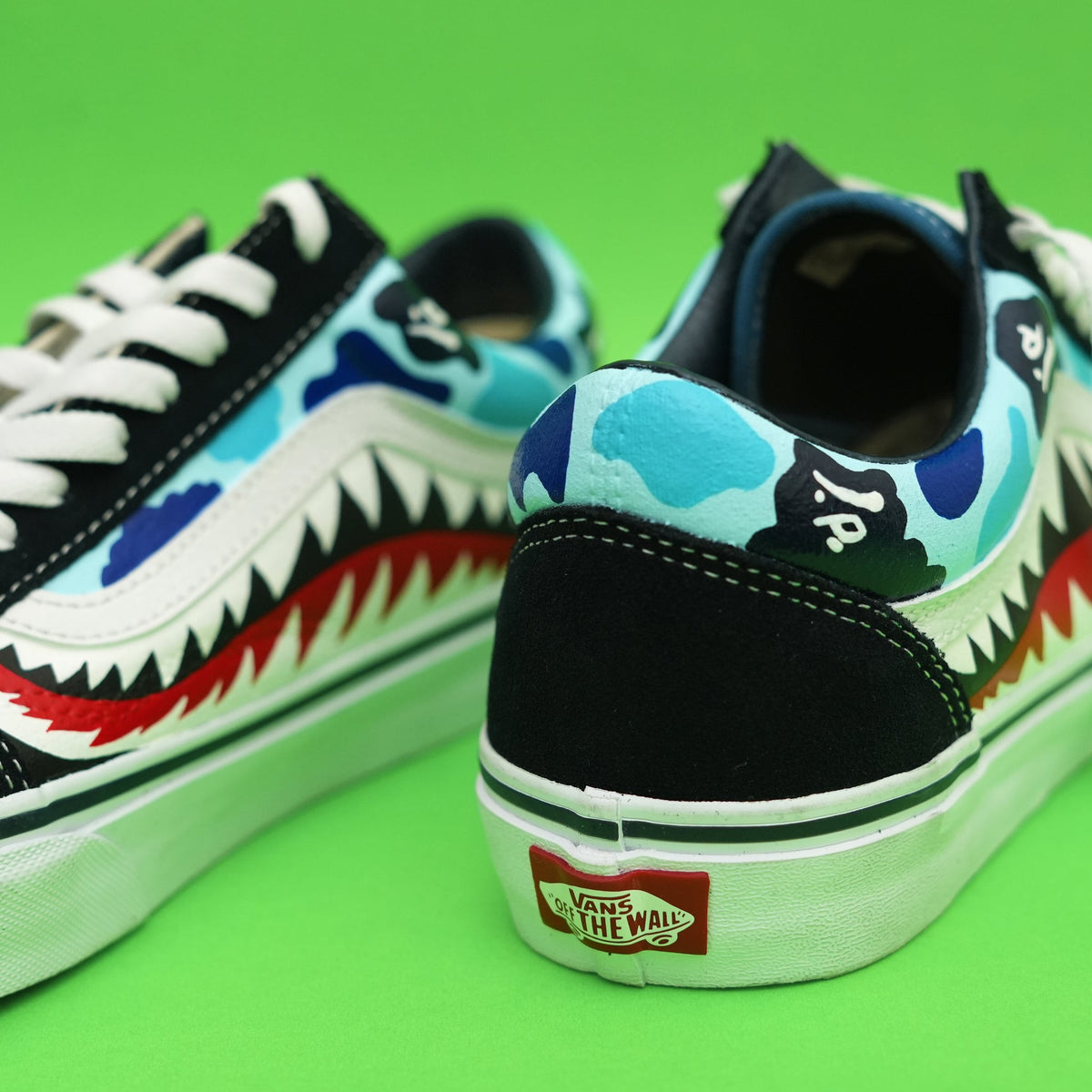 Vans sneakers with blue camo pattern, shark teeth graphic, and white laces on green background