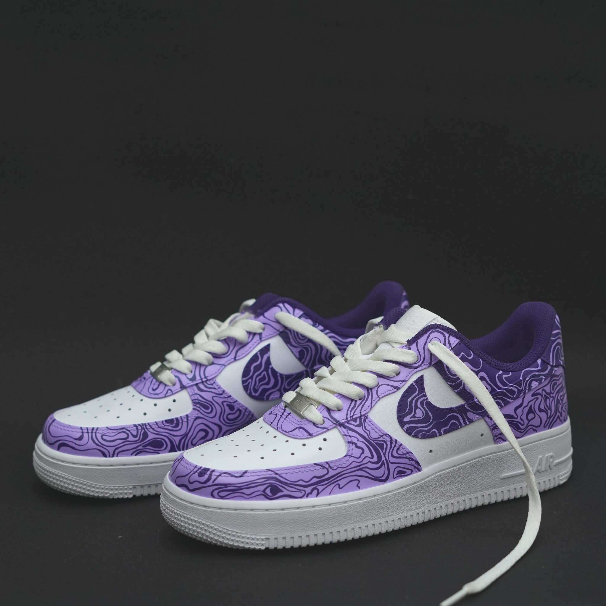 White and purple low-top streetwear sneakers with abstract pattern on a black background