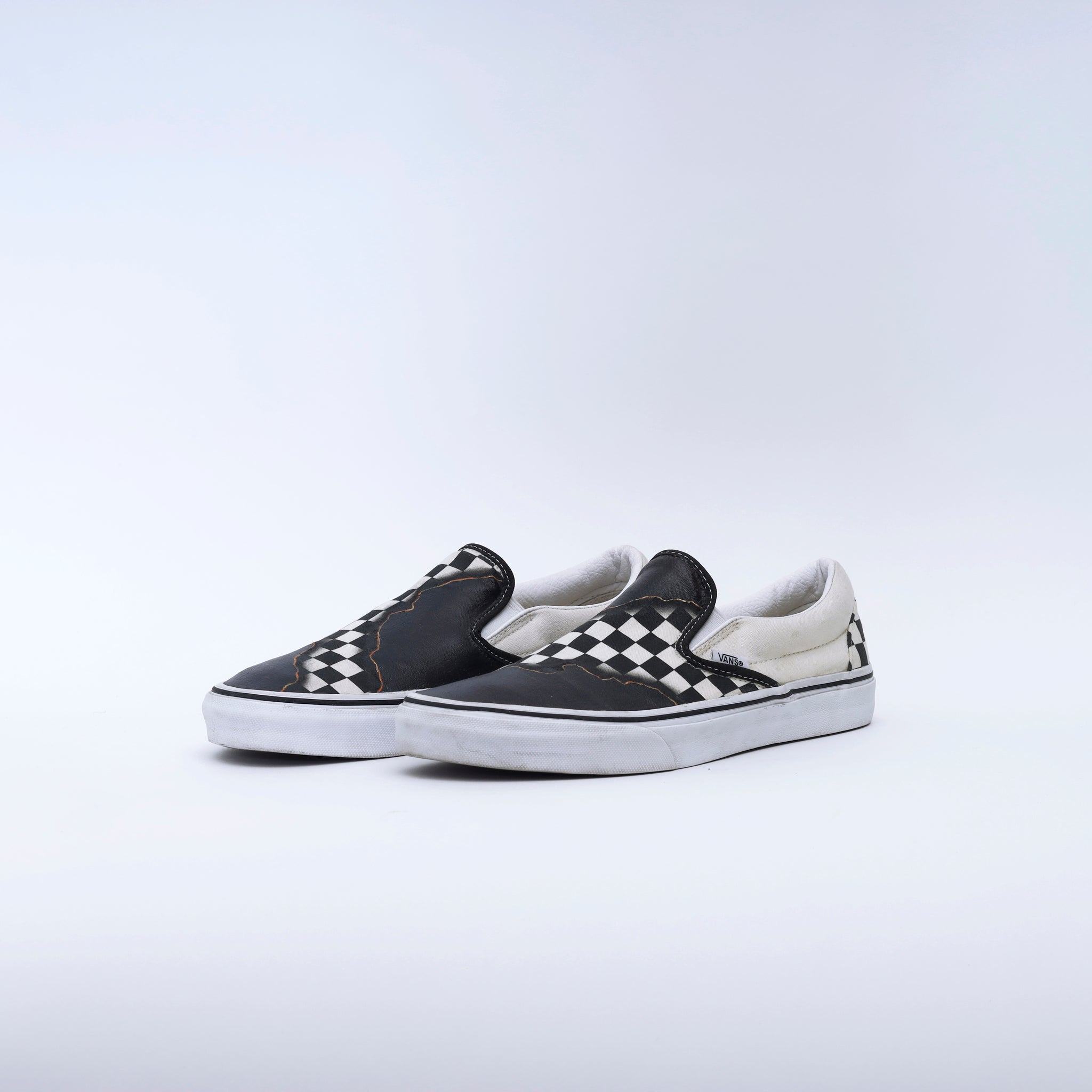 Black and white checkered slip-on sneakers with worn detailing on a white background