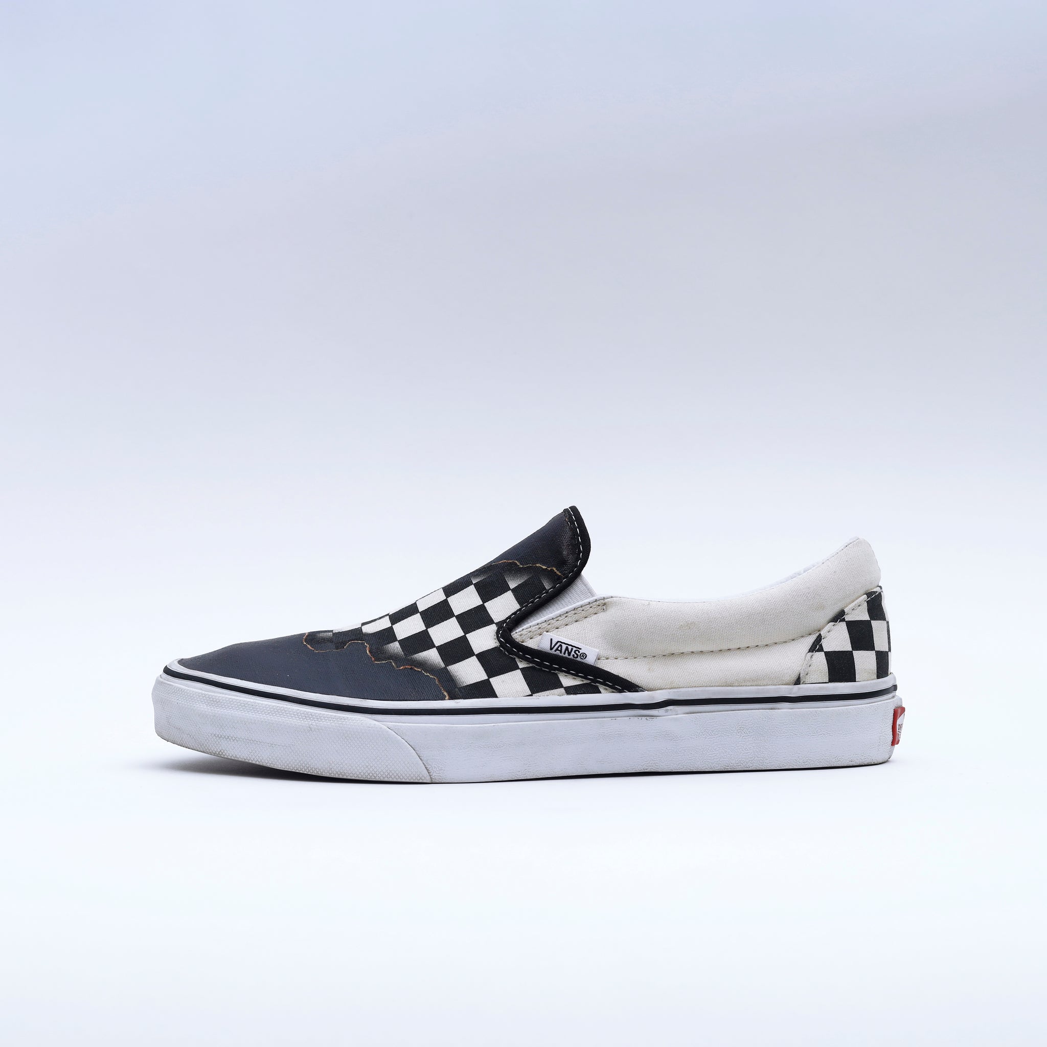 Worn black and white checkerboard Vans slip-on sneaker on a plain background