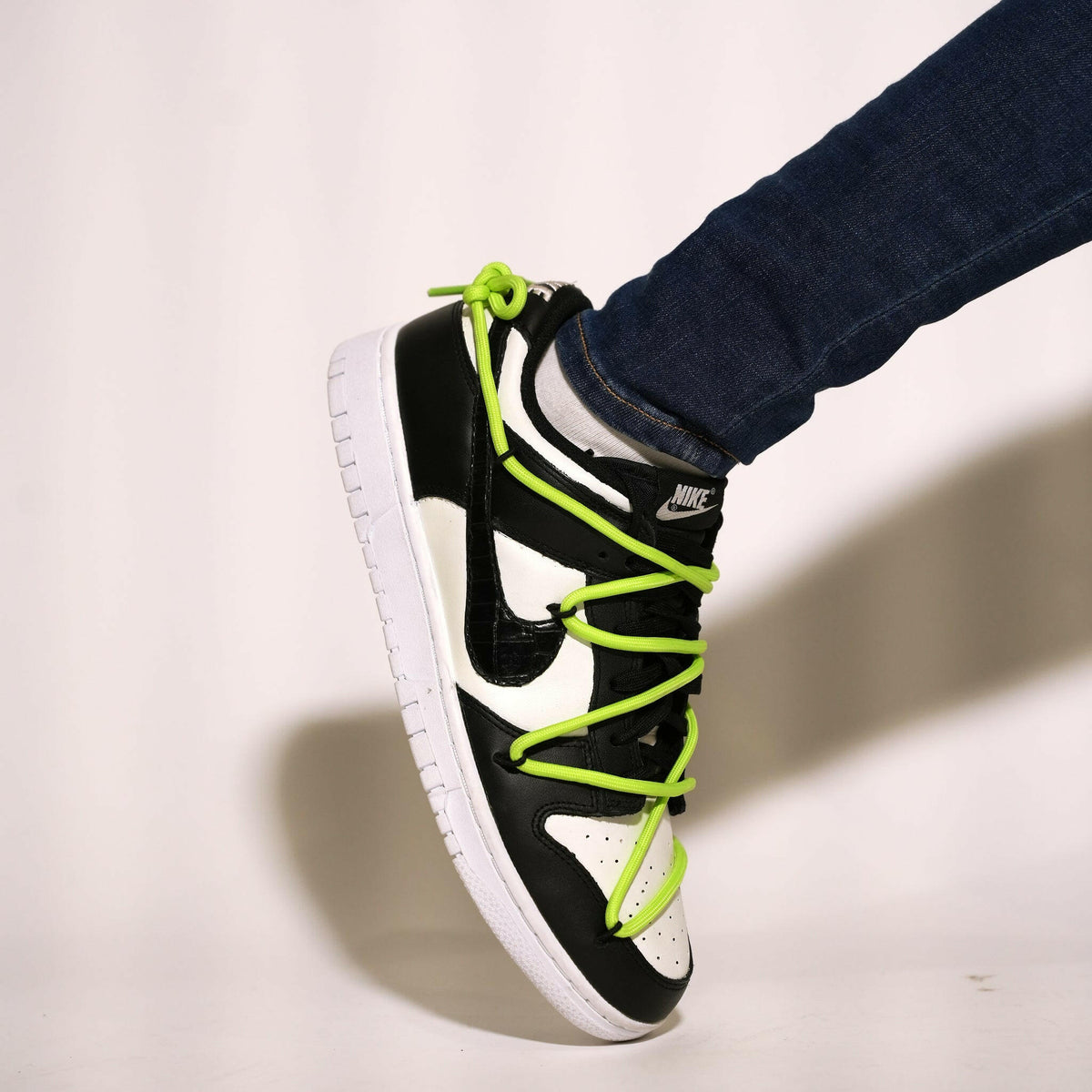 Black and white Nike sneaker with neon green laces, worn with jeans for streetwear style