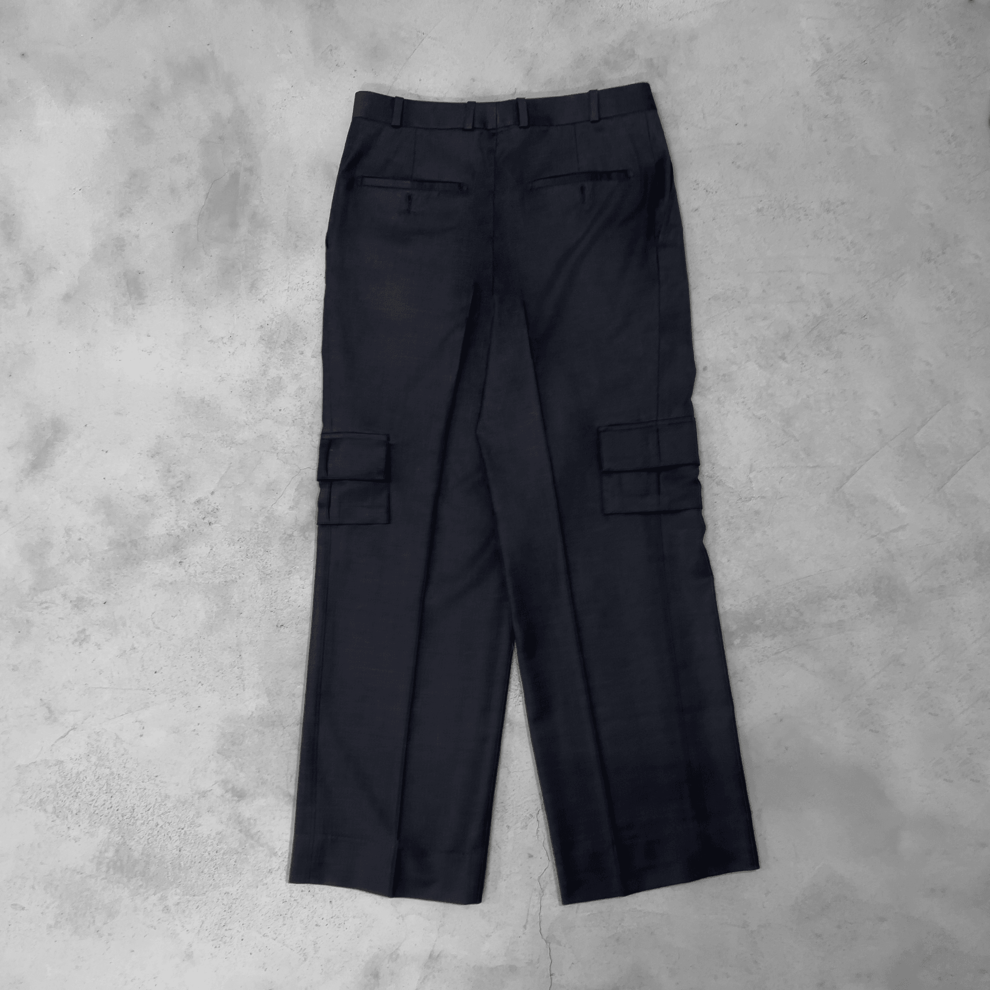 Back view of dark grey cargo pants with pockets, streetwear style on concrete background