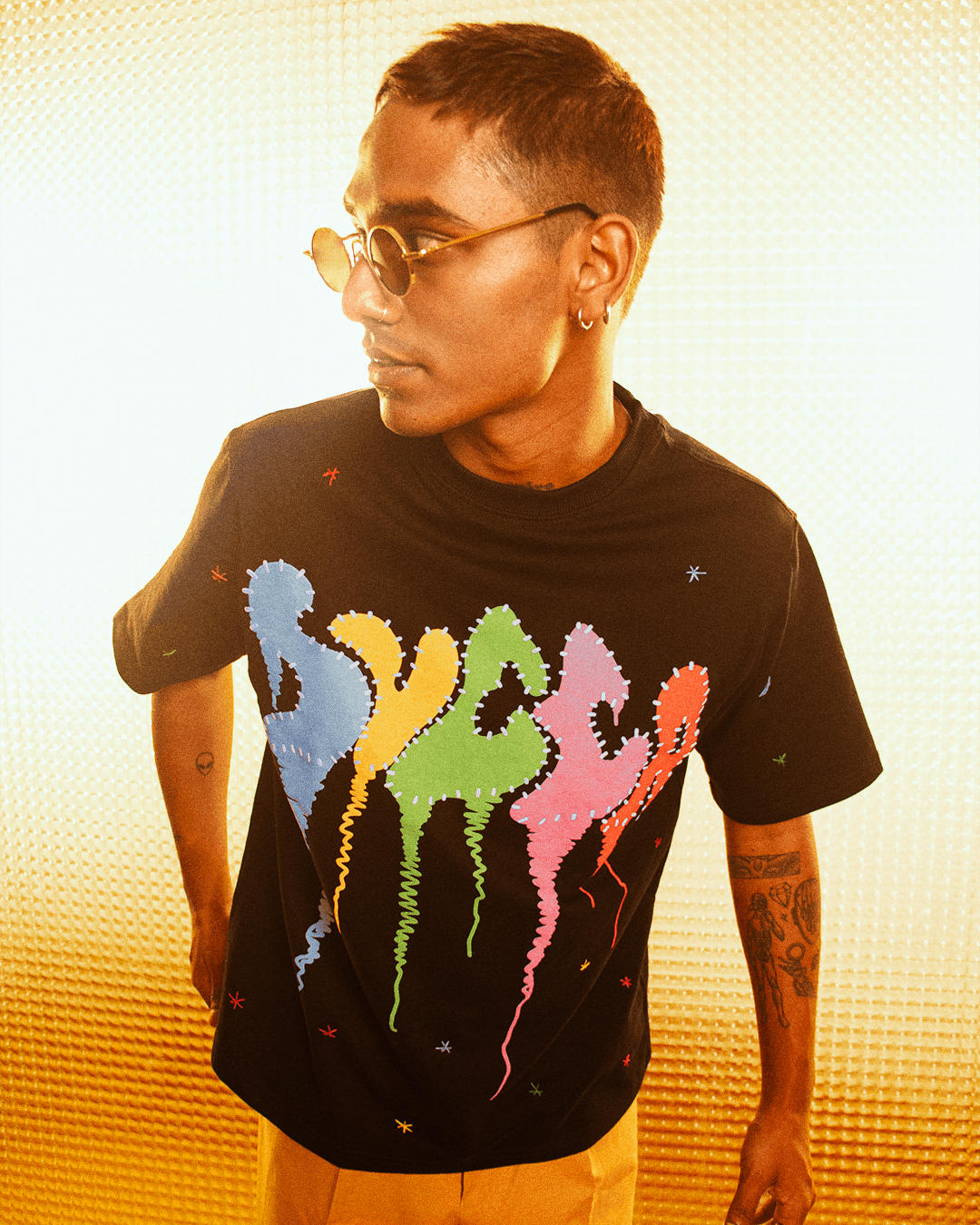 Man in streetwear black graphic t-shirt with colorful drip design, round sunglasses, tattoos