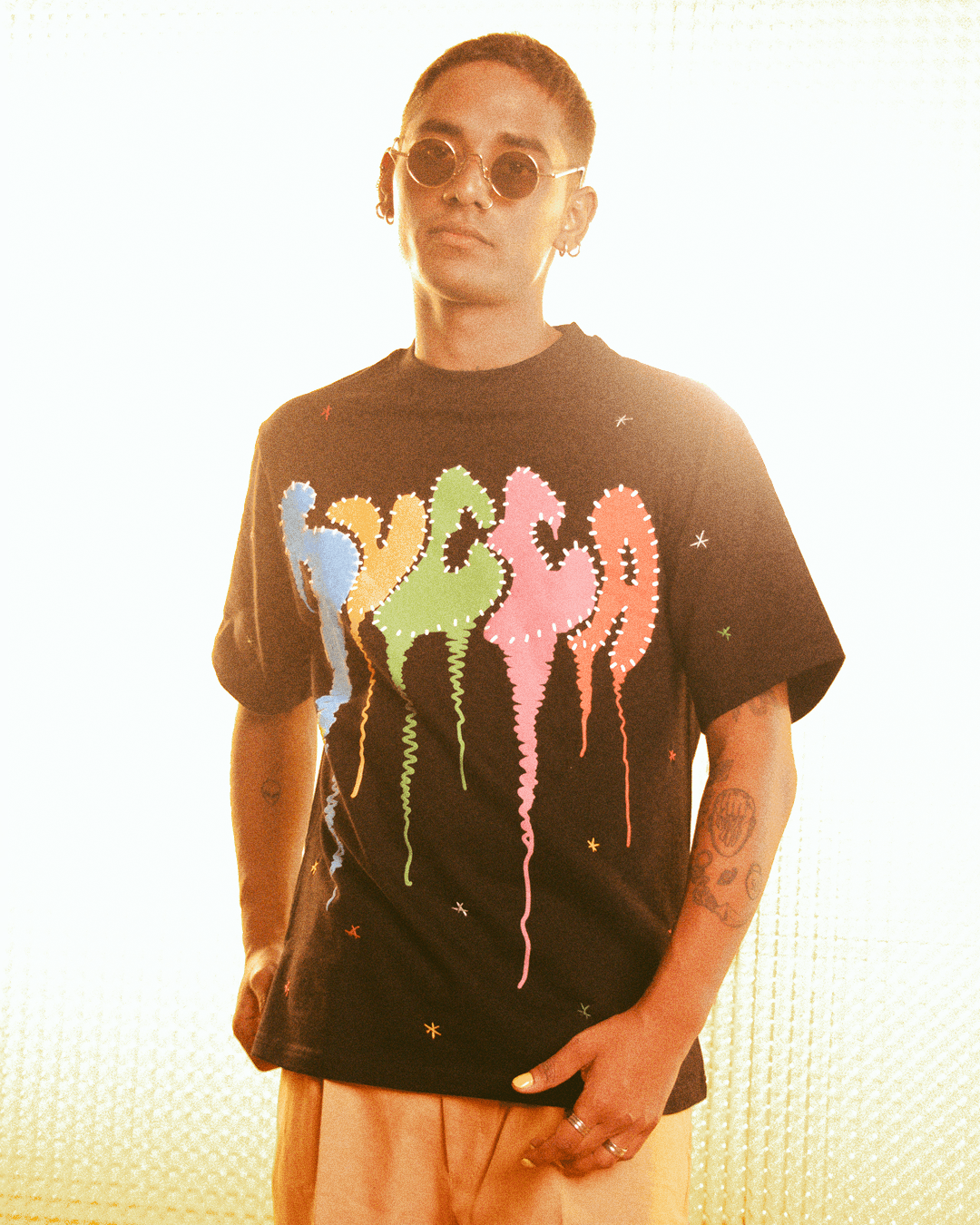 Man wearing round sunglasses and a black streetwear t-shirt with colorful abstract text graphic