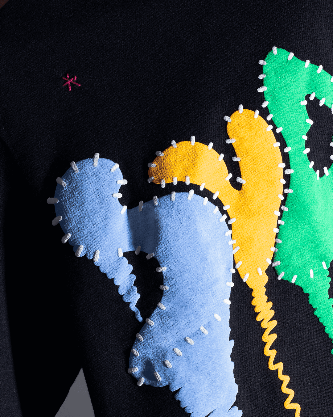 Streetwear graphic patch detail on black fabric, featuring blue, yellow, green shapes with visible white stitching