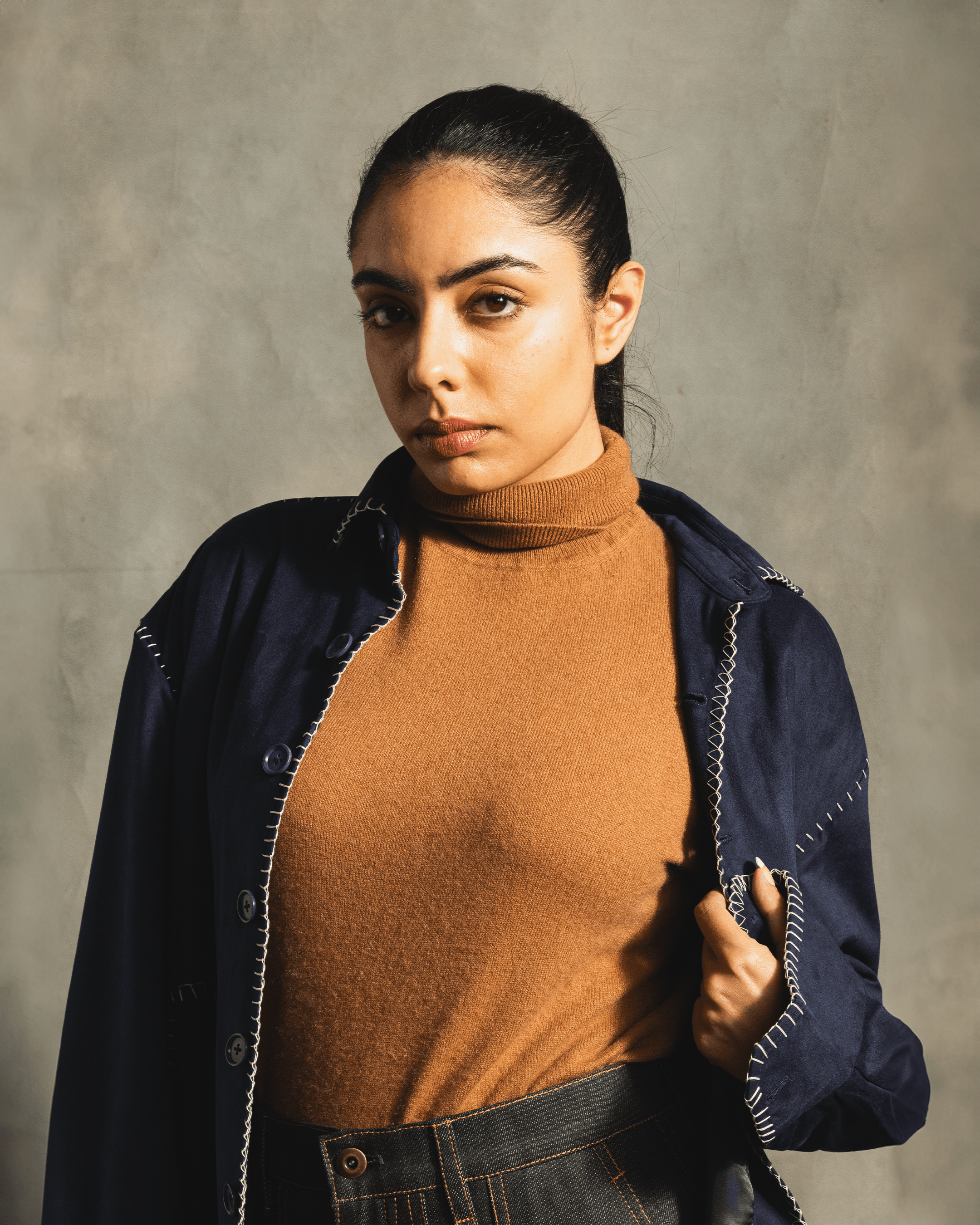 Woman in tan turtleneck and dark denim jacket with white contrast flatlock stitching, streetwear fashion