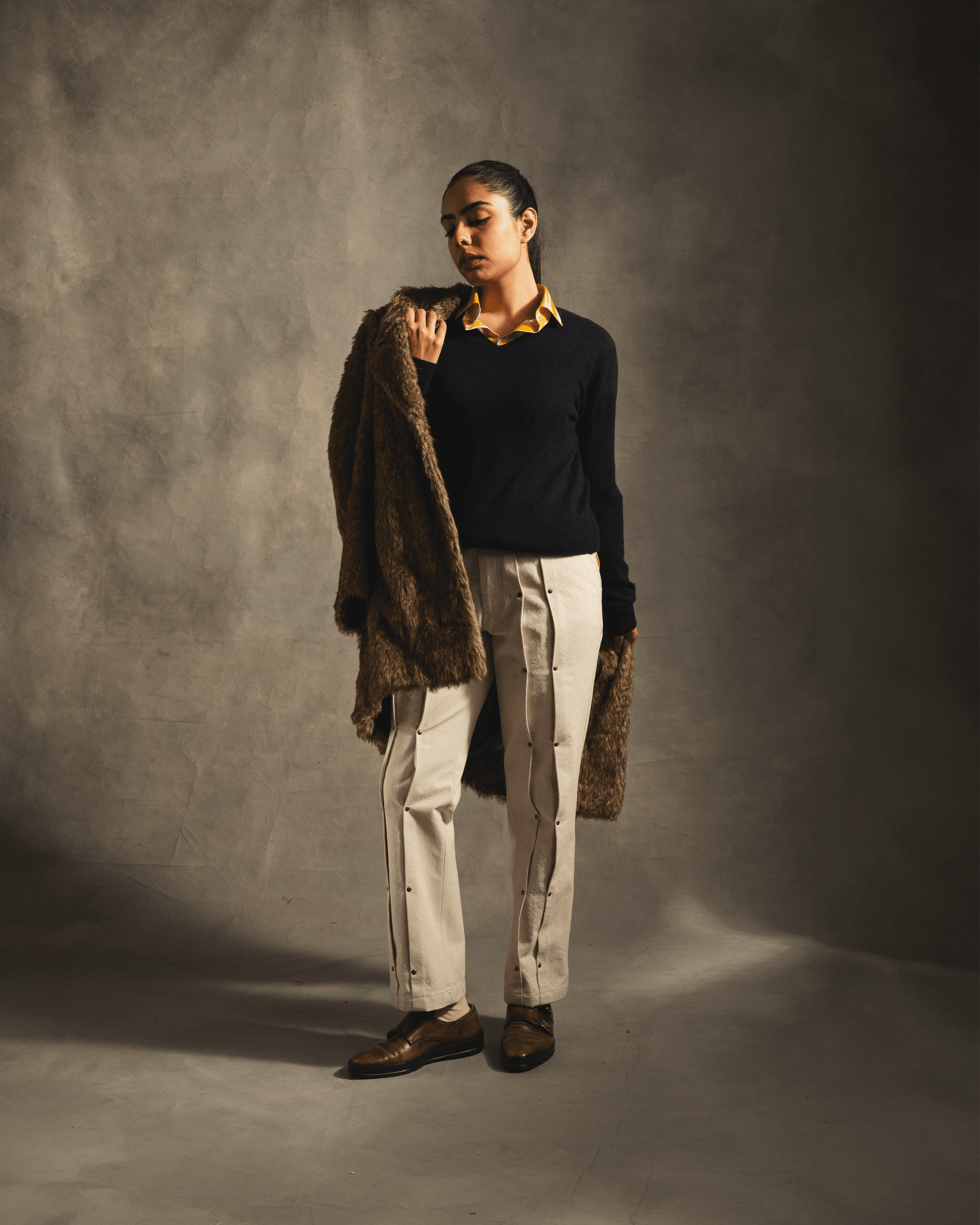 Woman in streetwear holding brown fur coat, wearing beige pants and black sweater