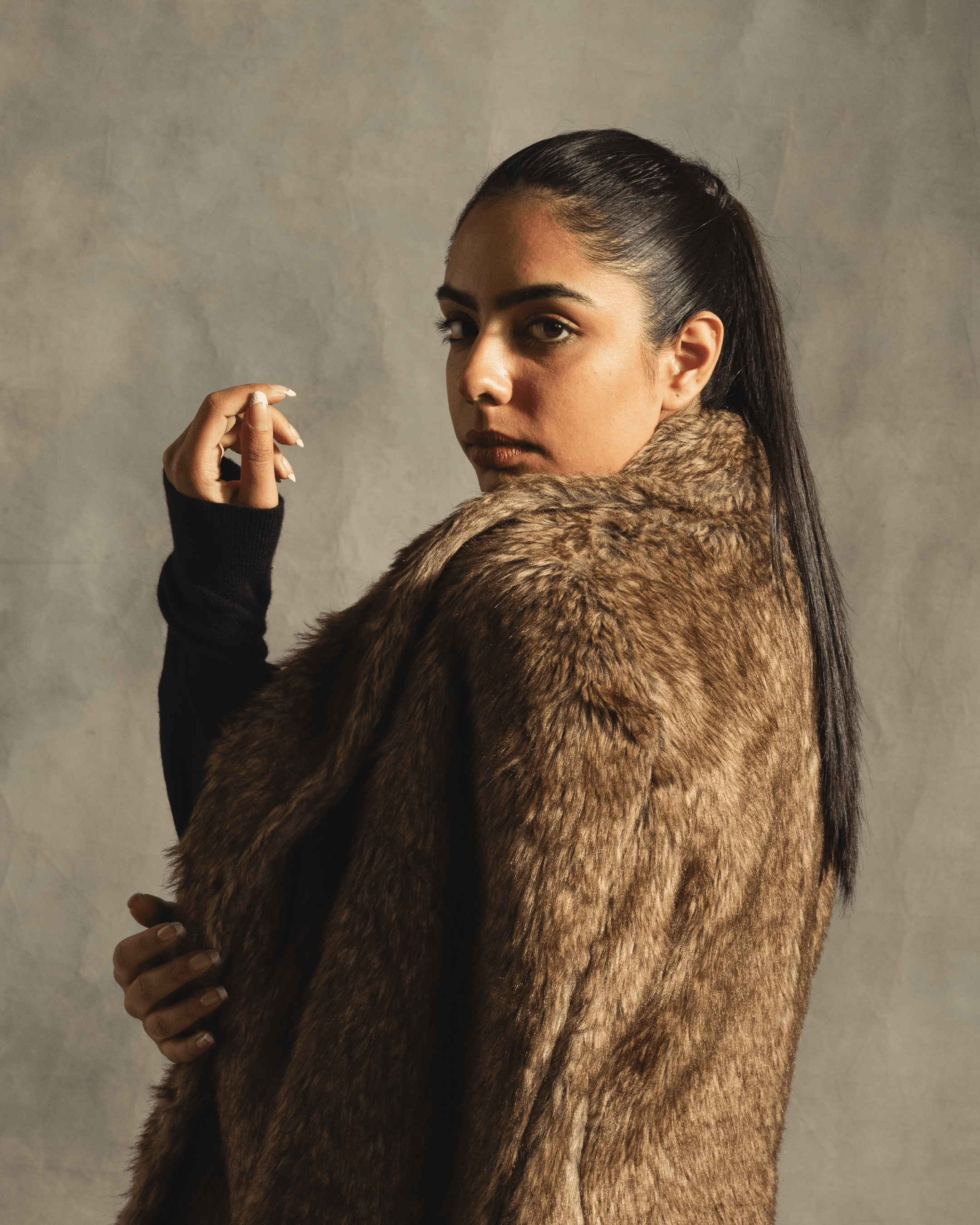Woman in brown faux fur coat posing against neutral background, streetwear fashion style