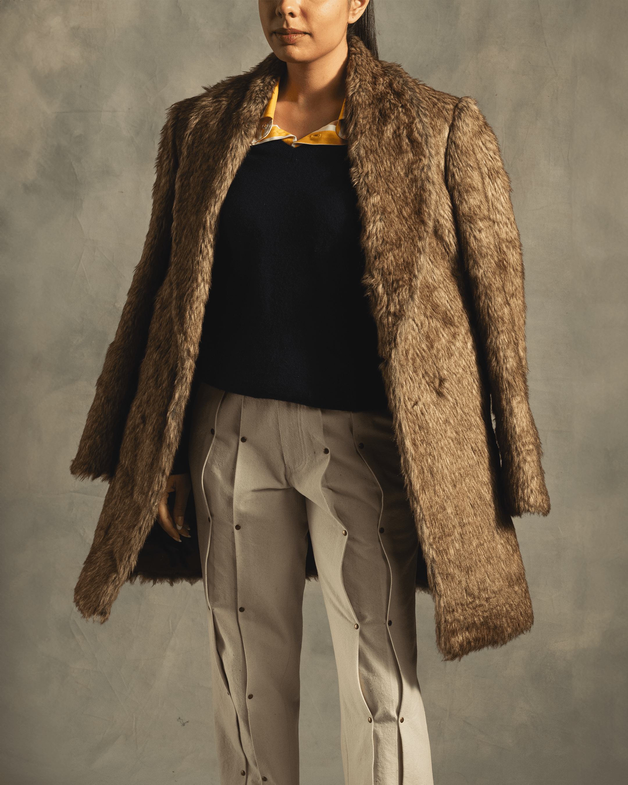 Woman wearing brown faux fur coat, black top, and beige streetwear pants.