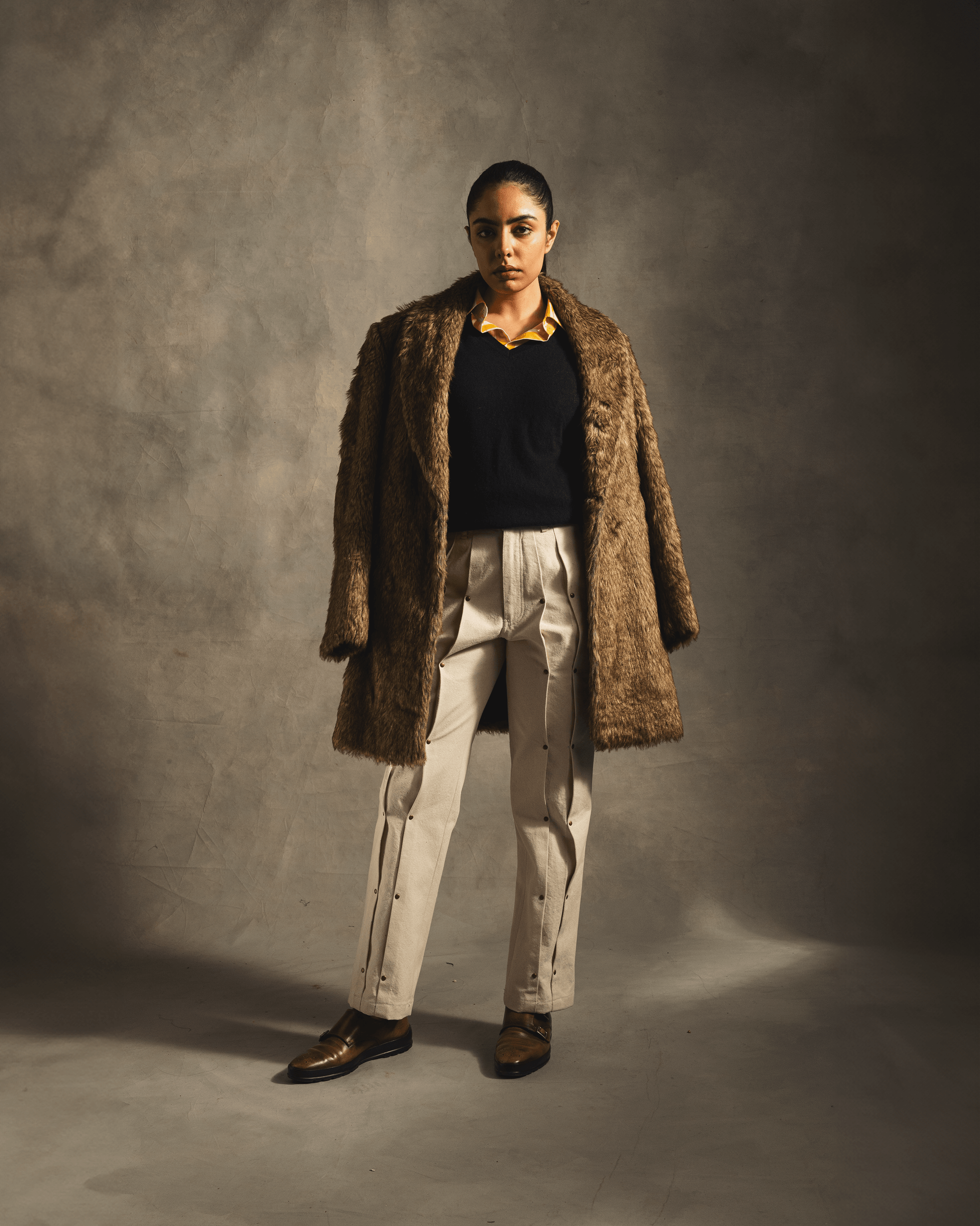 Woman in a brown faux fur coat with beige trousers and black sweater, studio shot